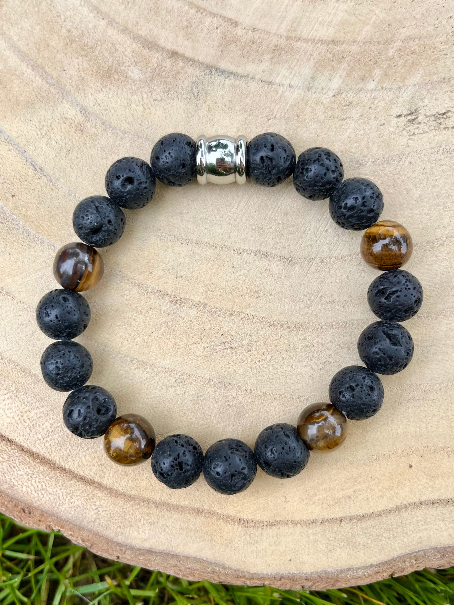 Bracelet ADAM, avec Pierre de Lave et Oeil de Tigre, exposé sur un rondin de bois.