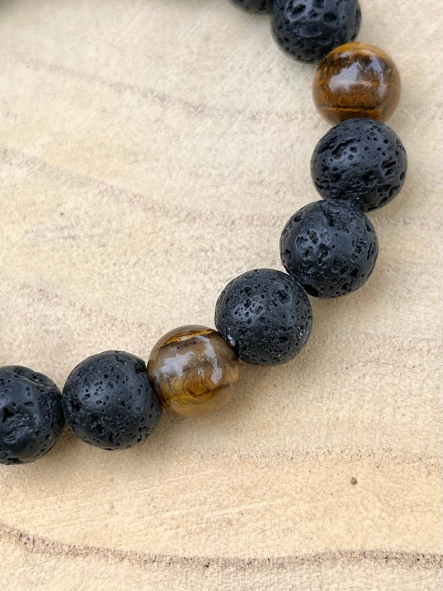 Bracelet ADAM, avec Pierre de Lave et Oeil de Tigre, exposé sur un rondin de bois.