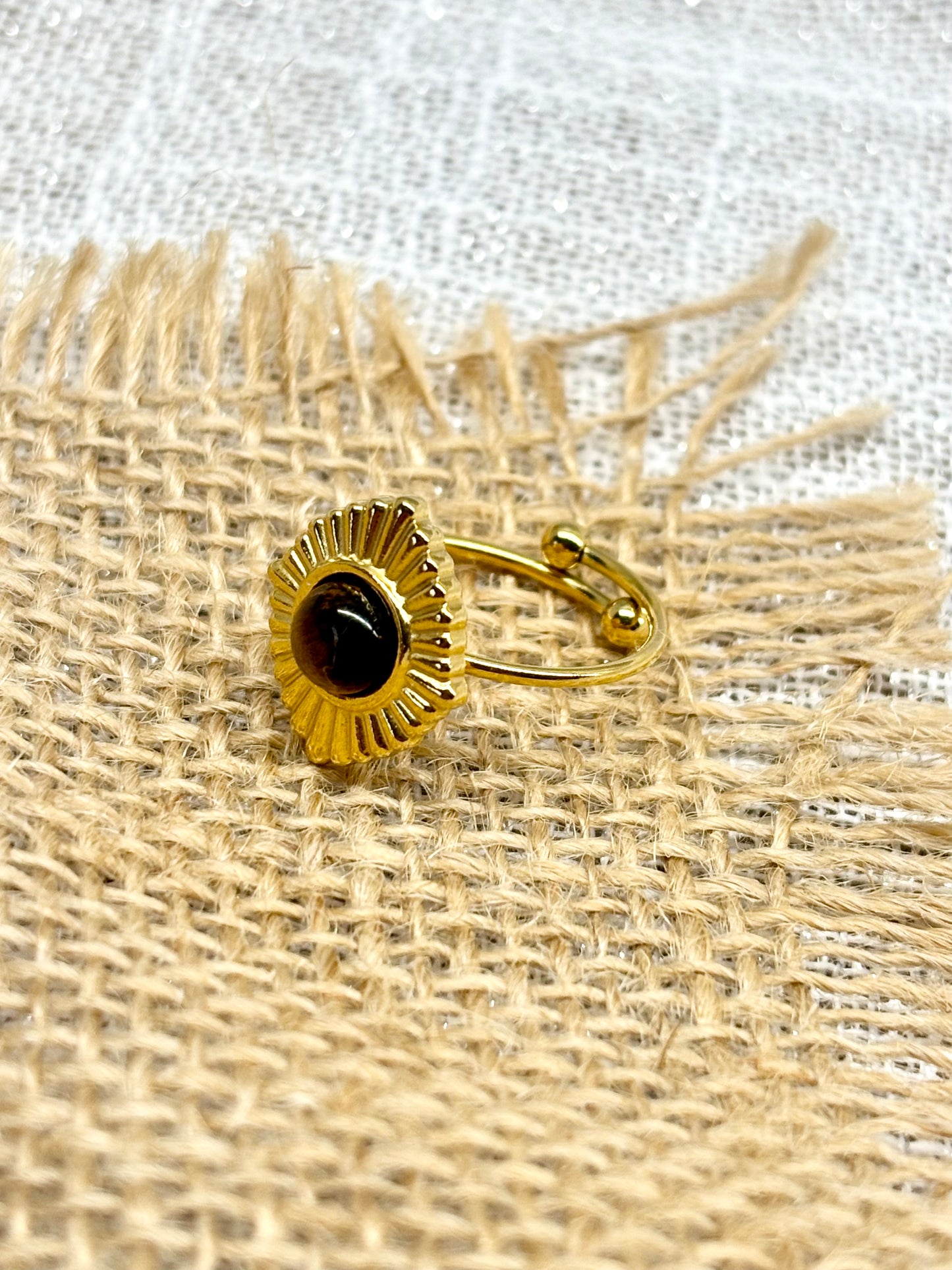 Bague ALYSÉE, de couleur dorée avec pierre d'Oeil de Tigre, exposée sur un fond en lin et toile de jute.