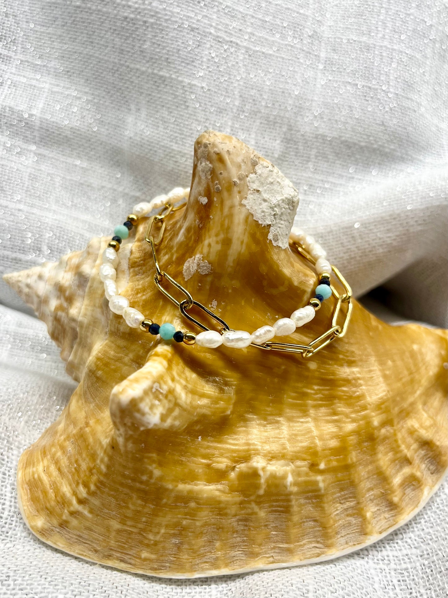 Bracelet ARIANA, avec pierre d'Amazonite, Saphir et Perle de Culture, exposé sur un coquillage.