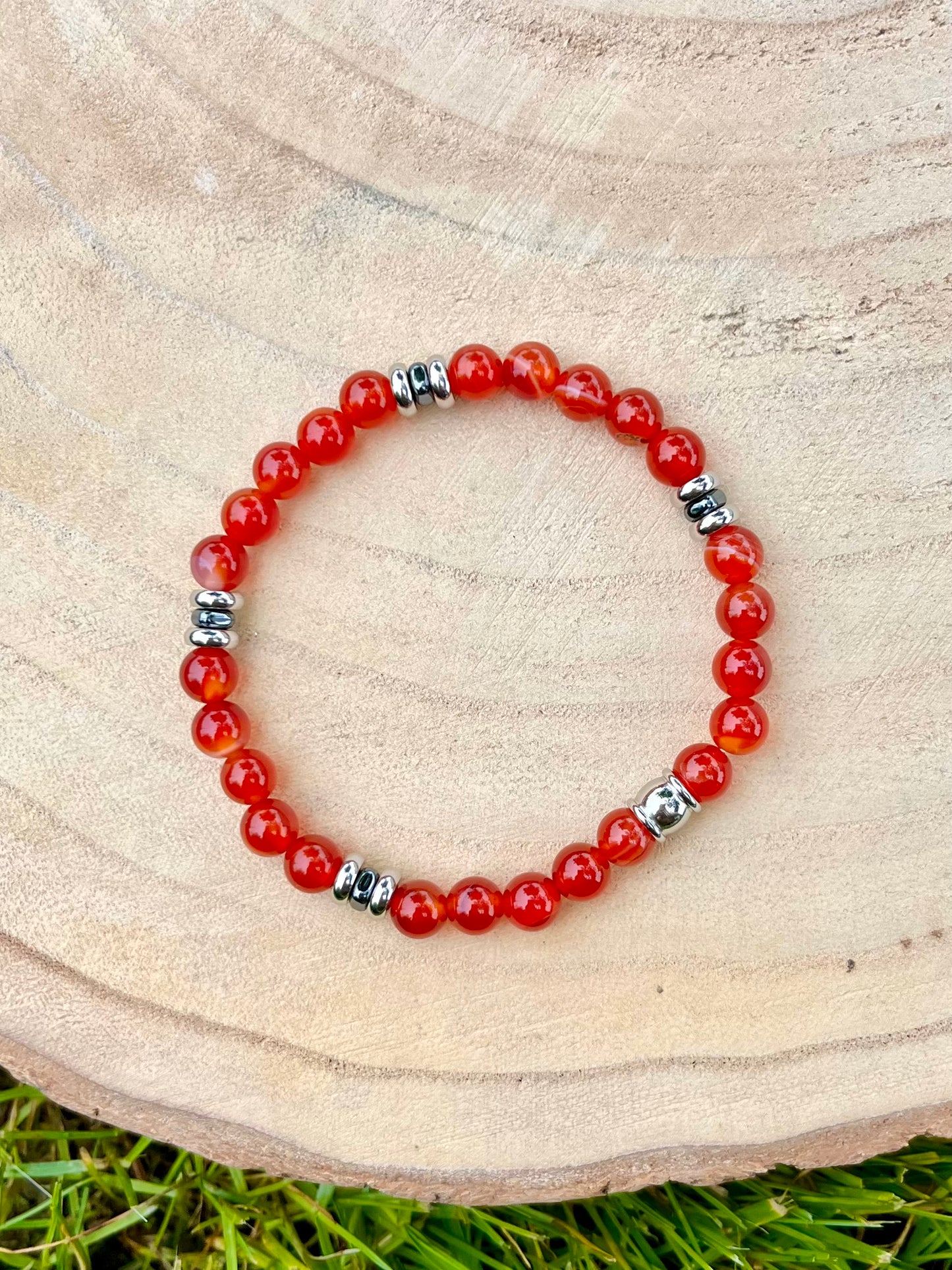 Bracelet CAMILLE, avec pierres de Cornaline et d'Hématite, exposé sur un rondin de bois.
