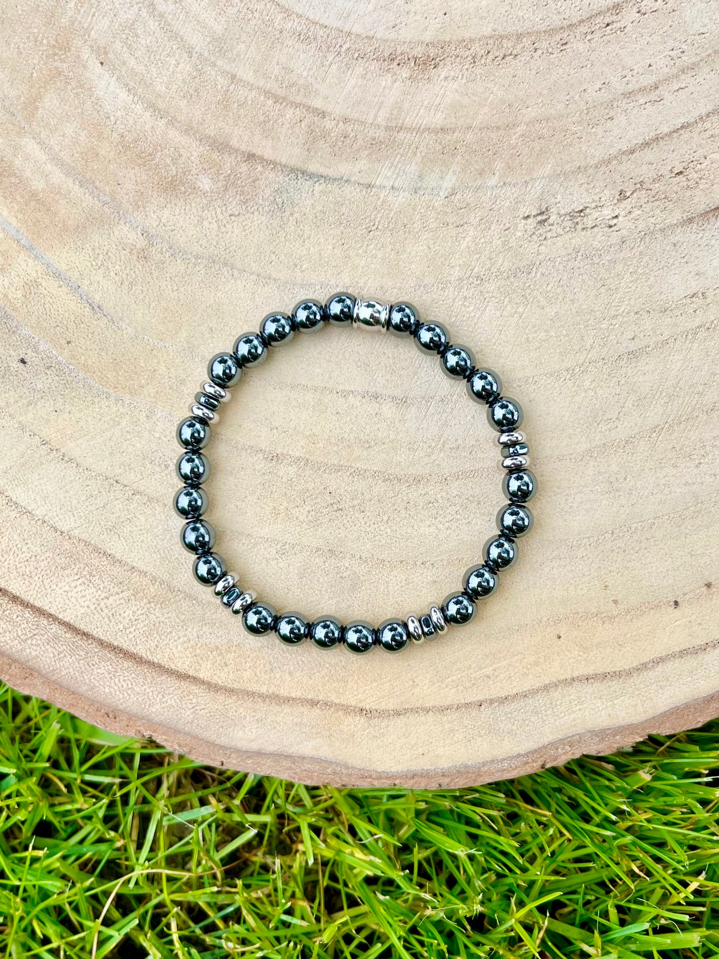 Bracelet CAMILLE, avec pierres d'Hématite, exposé sur un rondin de bois.