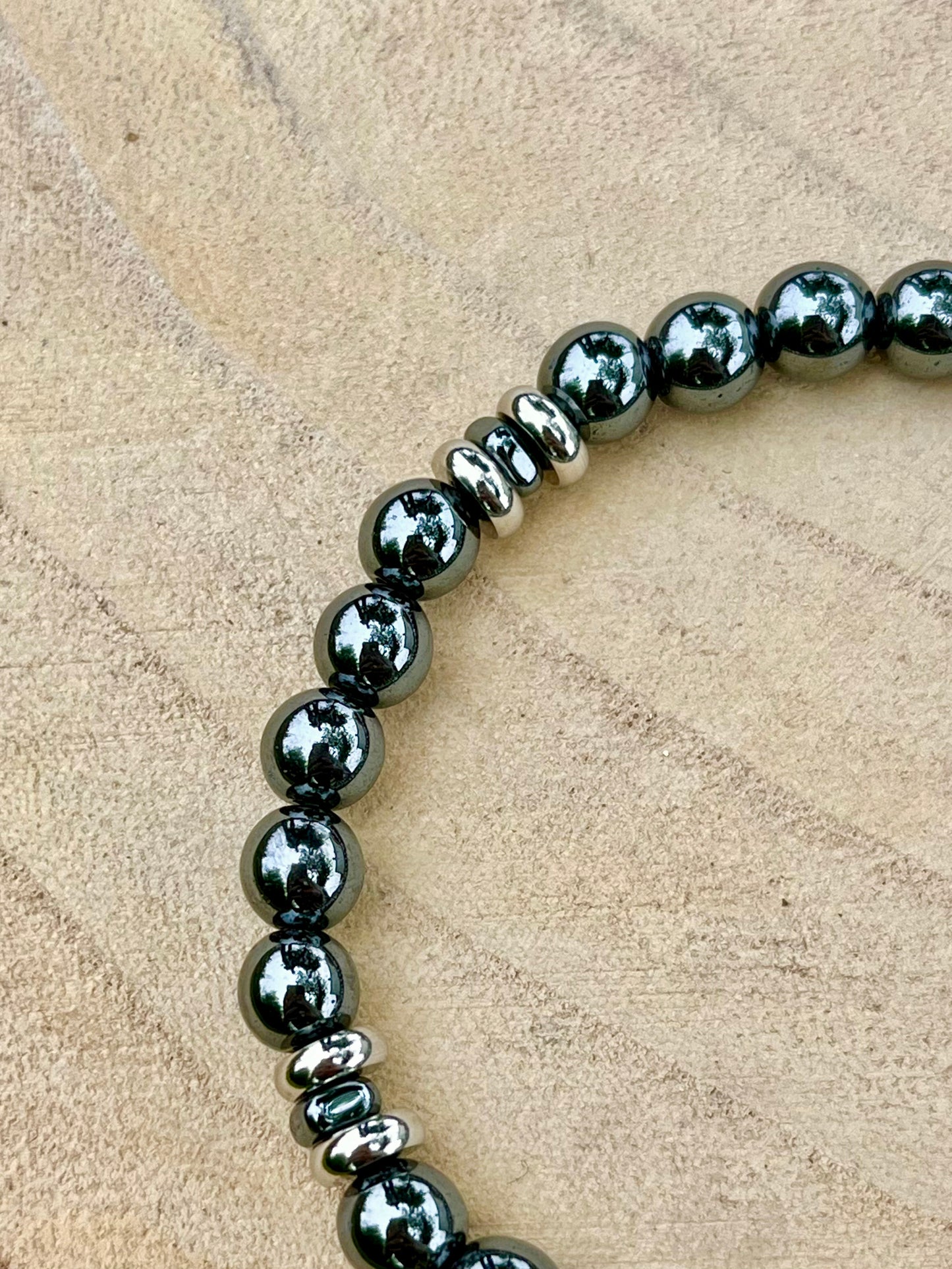 Bracelet CAMILLE, avec pierres d'Hématite, exposé sur un rondin de bois.