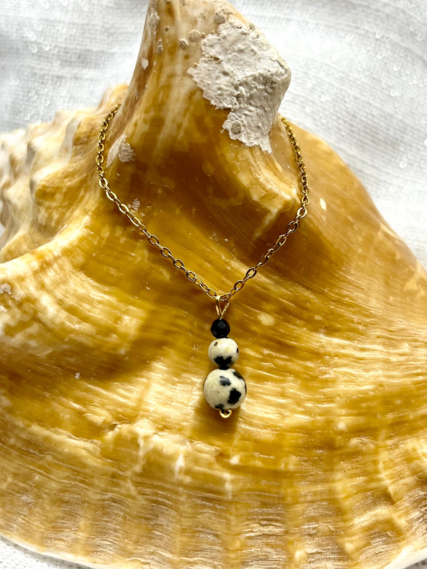 Collier EMMA, avec pierres de Jaspe Dalmatien et de Tourmaline Noire, exposé sur un coquillage.