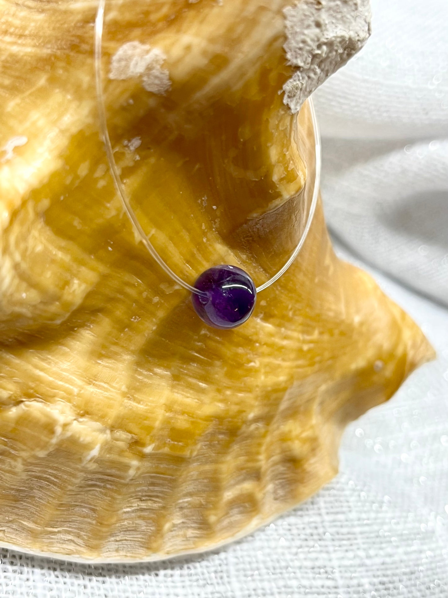 Collier EMY en pierre d'Améthyste, exposé sur un coquillage.
