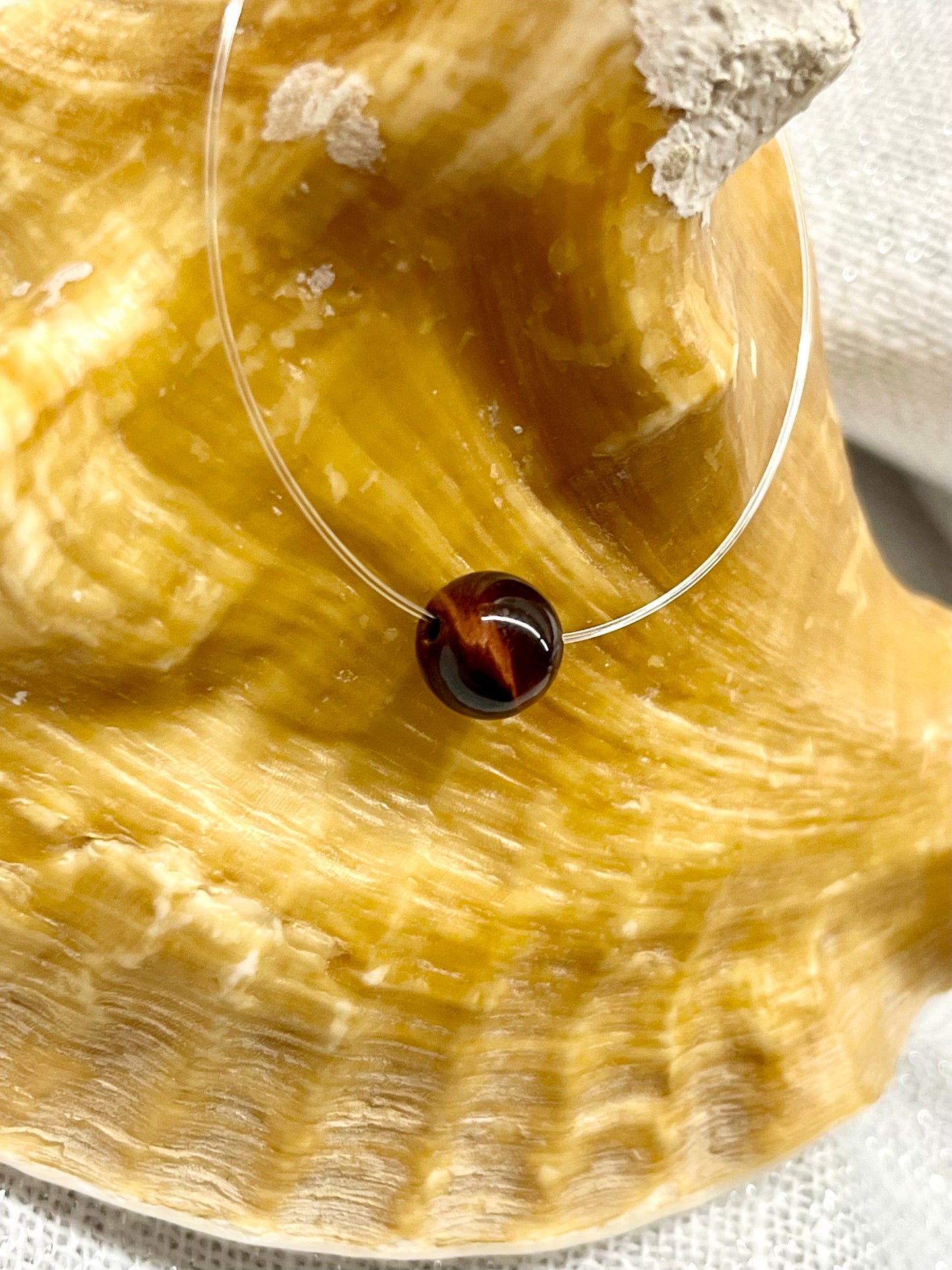 Collier EMY avec pierre d'Oeil de Taureau, exposé sur un coquillage.