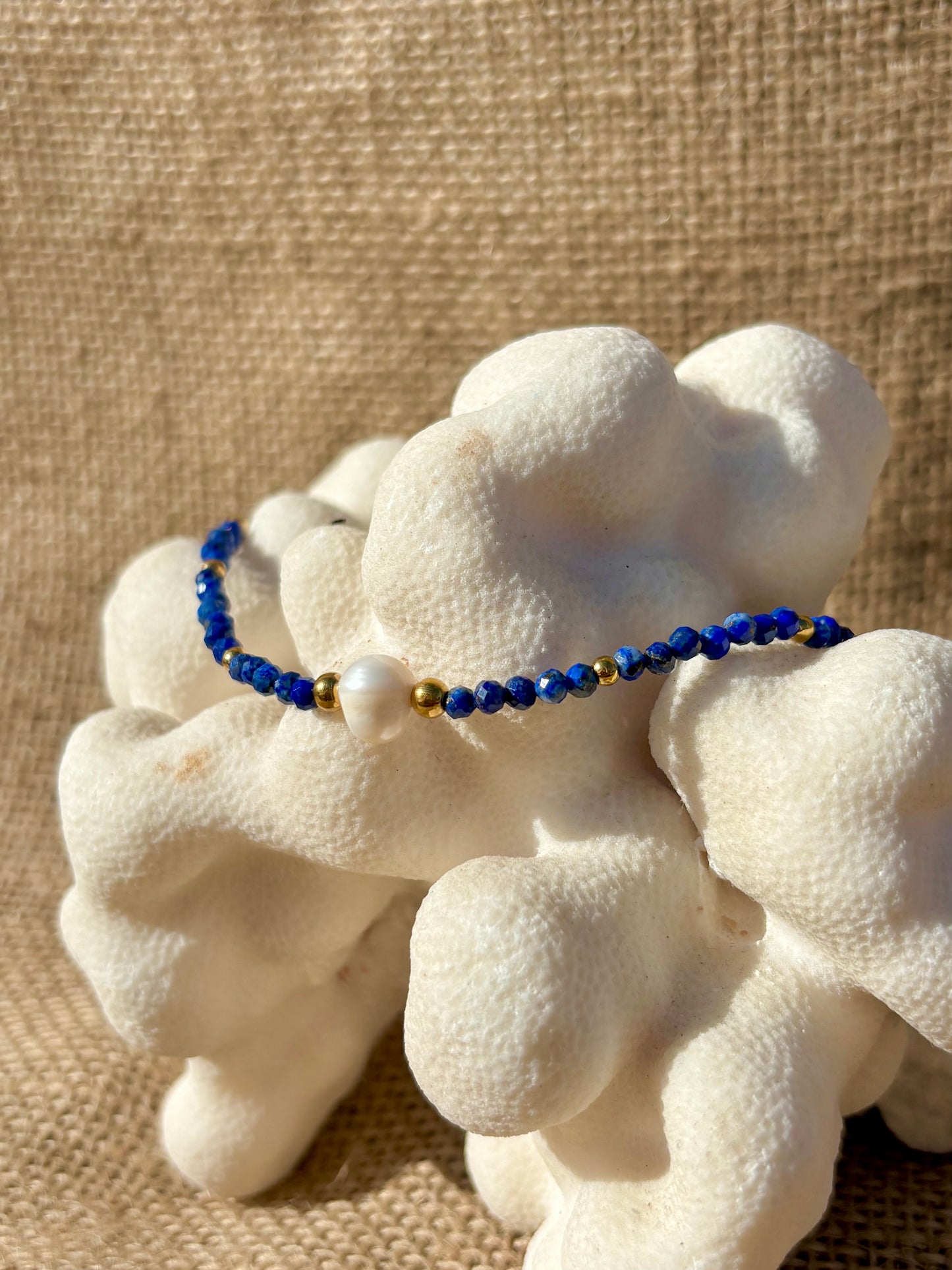 Vue latérale du bracelet ÈVE en perles de Lapis-Lazuli facettées et d’une perle de culture, sur un support en forme de corail blanc.