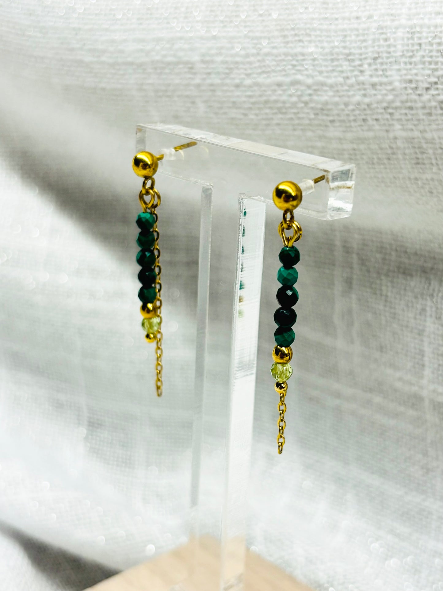 Boucles d'oreille JULIETTE, avec pierres de Malachite et de Péridot, exposées sur un fond en lin.