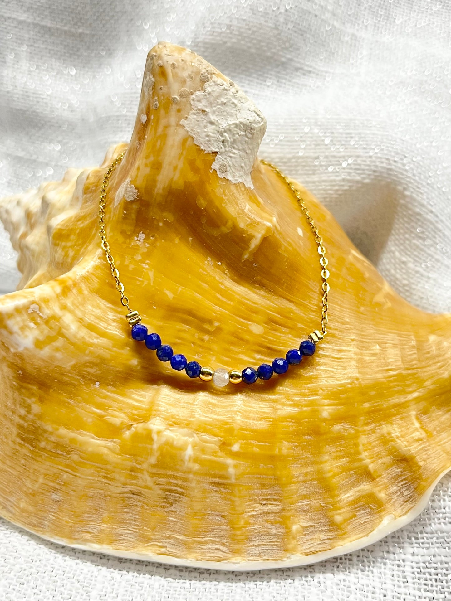 Collier JULIE, avec pierres de Lapis-Lazuli et de Labradorite, exposé sur un coquillage.