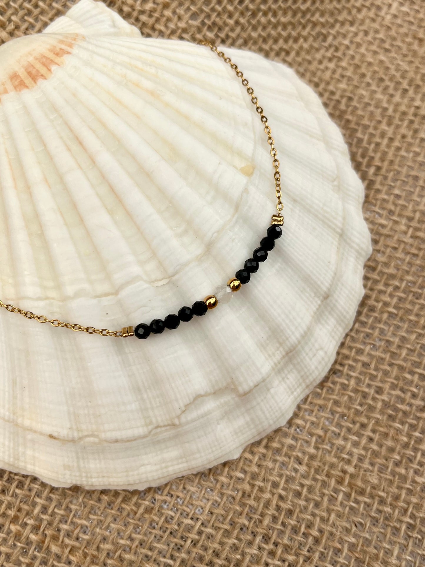 Collier JULIE, avec pierres de Tourmaline Noire et Pierre de Lune, exposé sur un coquillage.