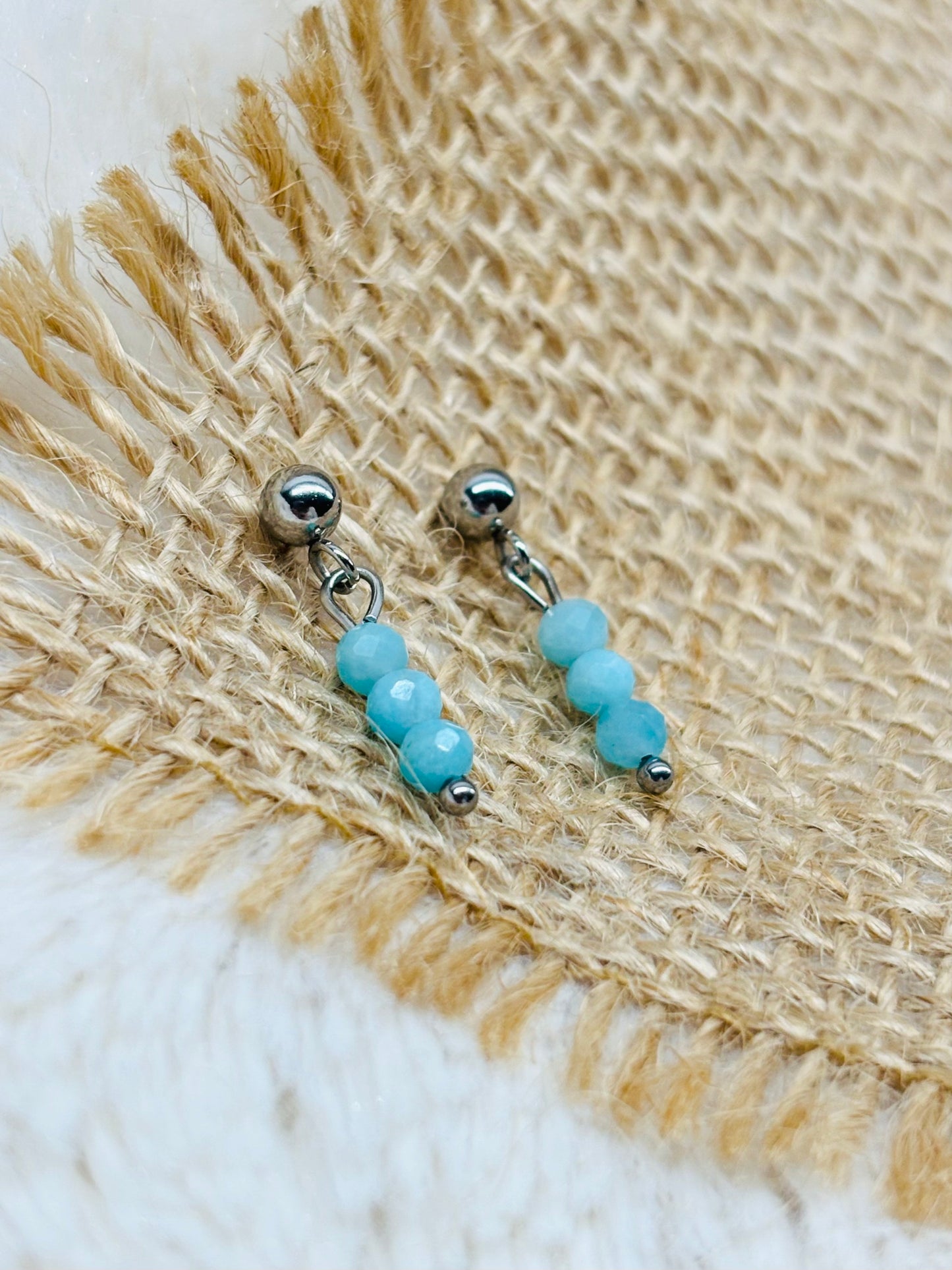 Boucles d'oreille LALY, avec pierres d'Amazonite, exposées sur de la toile de jute.