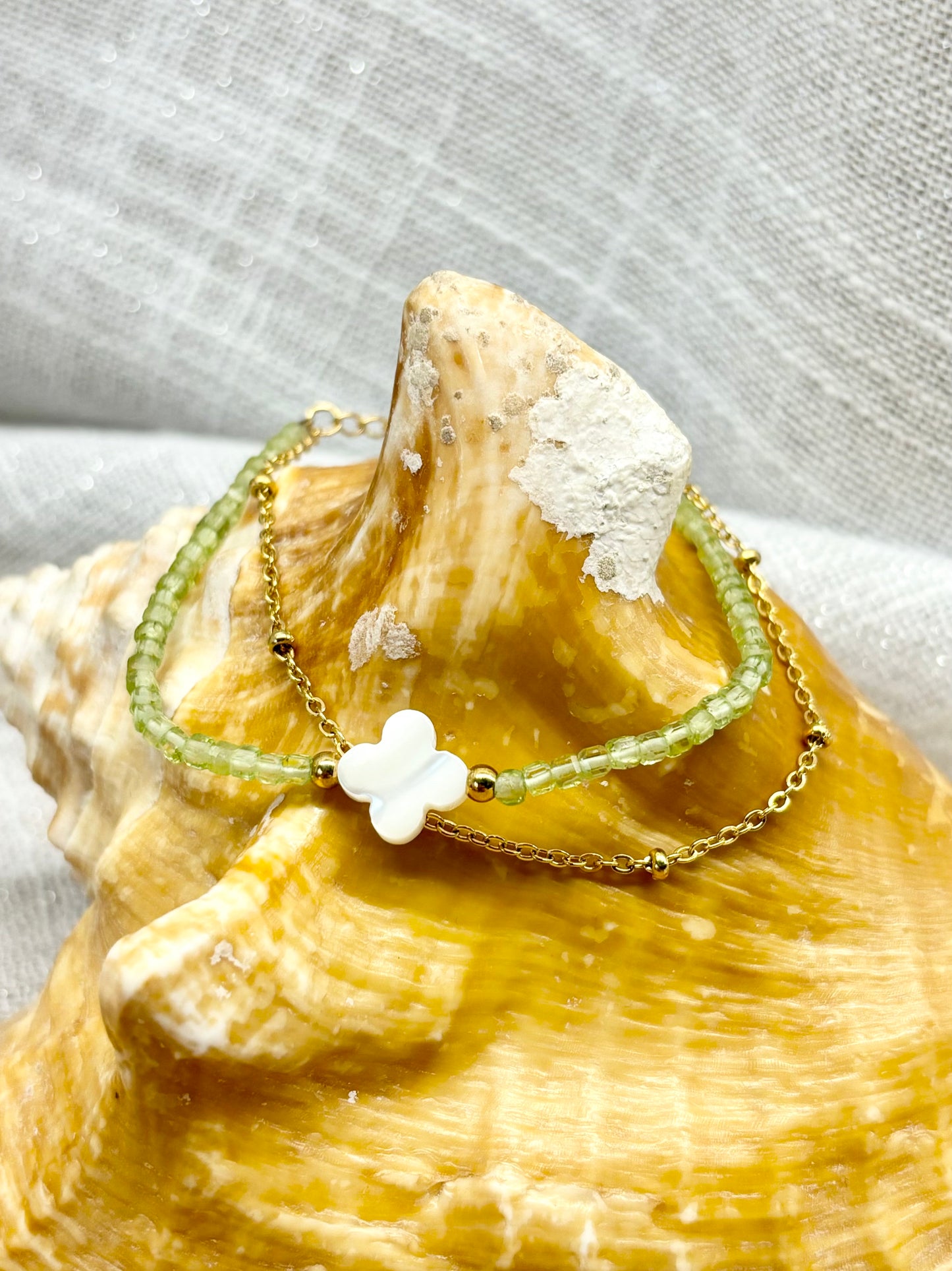 Bracelet LINA, avec pierres de Péridot et de Nacre, exposé sur un coquillage.