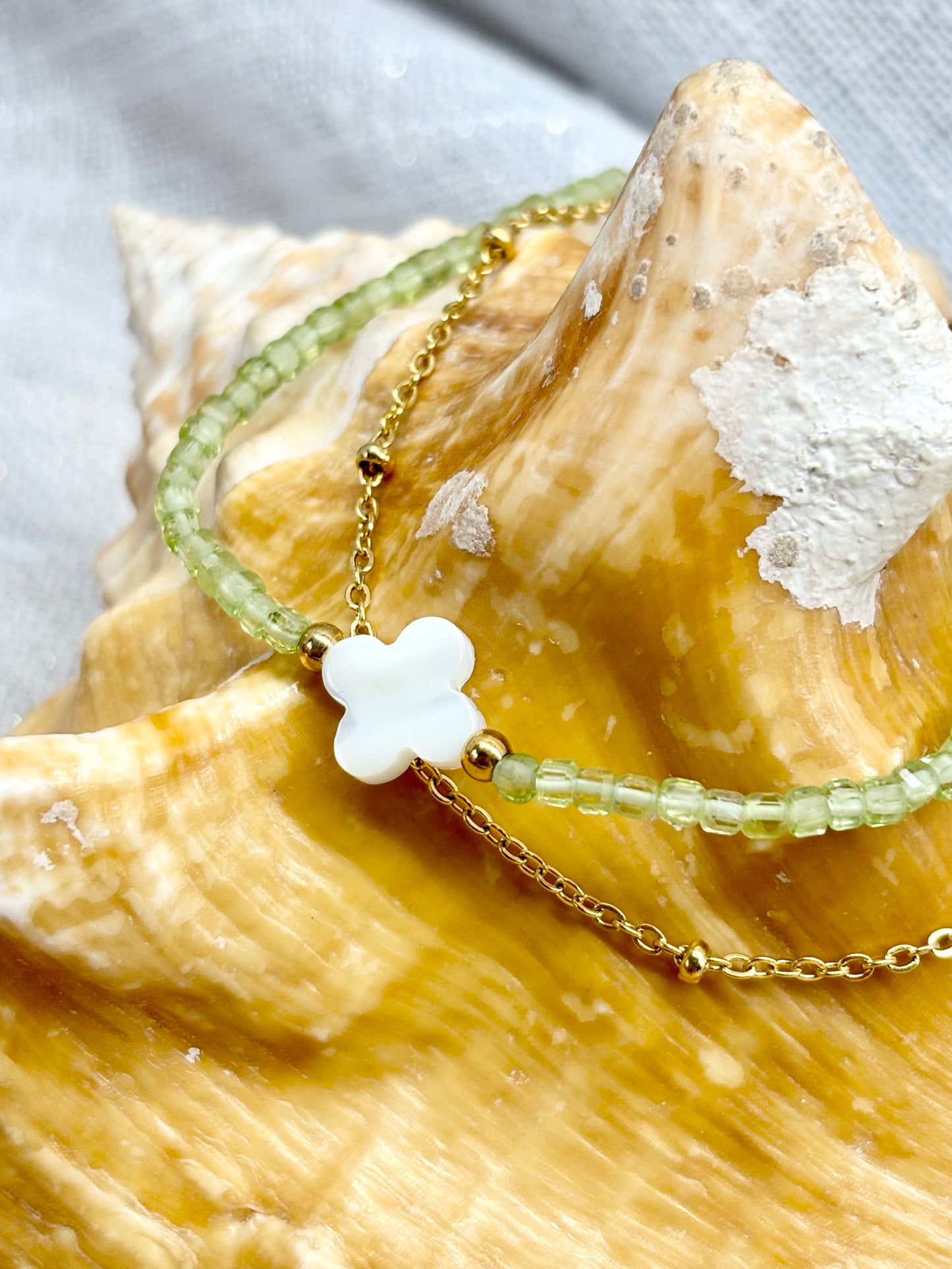 Bracelet LINA, avec pierres de Péridot et de Nacre, exposé sur un coquillage.
