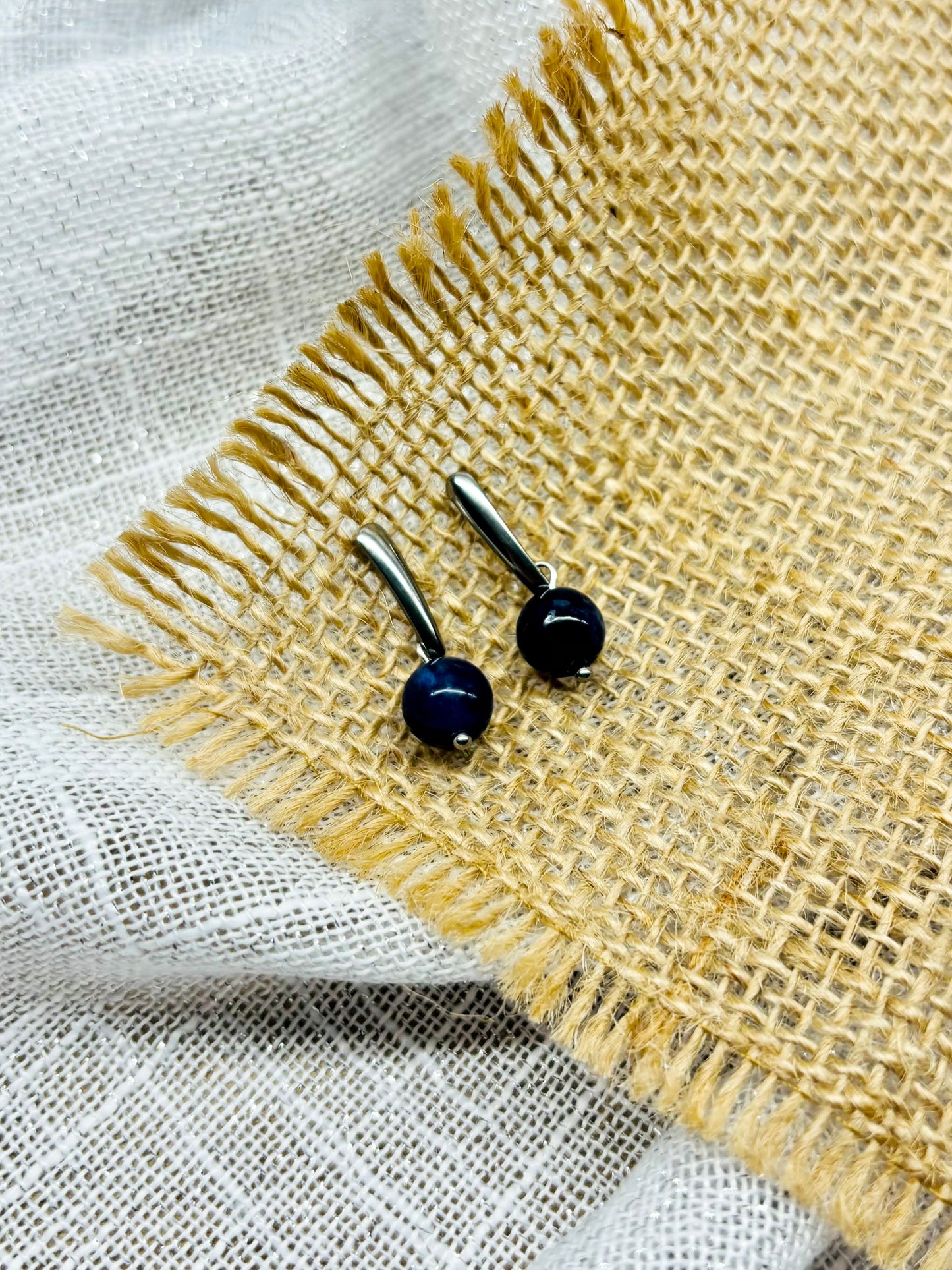 Boucles d'oreille MADELEINE, avec pierre de Sodalite, exposées sur de la toile de jute.