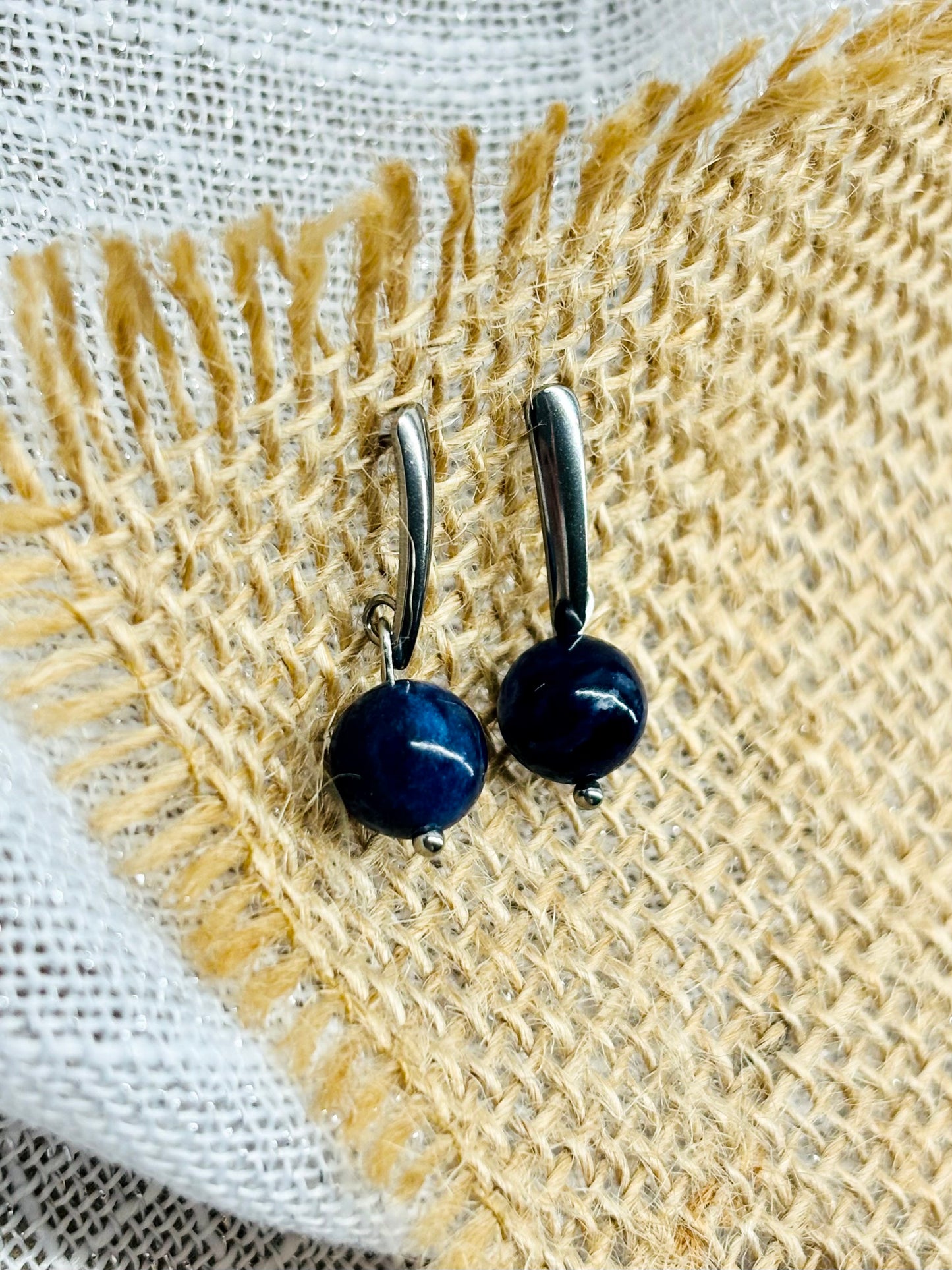 Boucles d'oreille MADELEINE, avec pierre de Sodalite, exposées sur de la toile de jute.