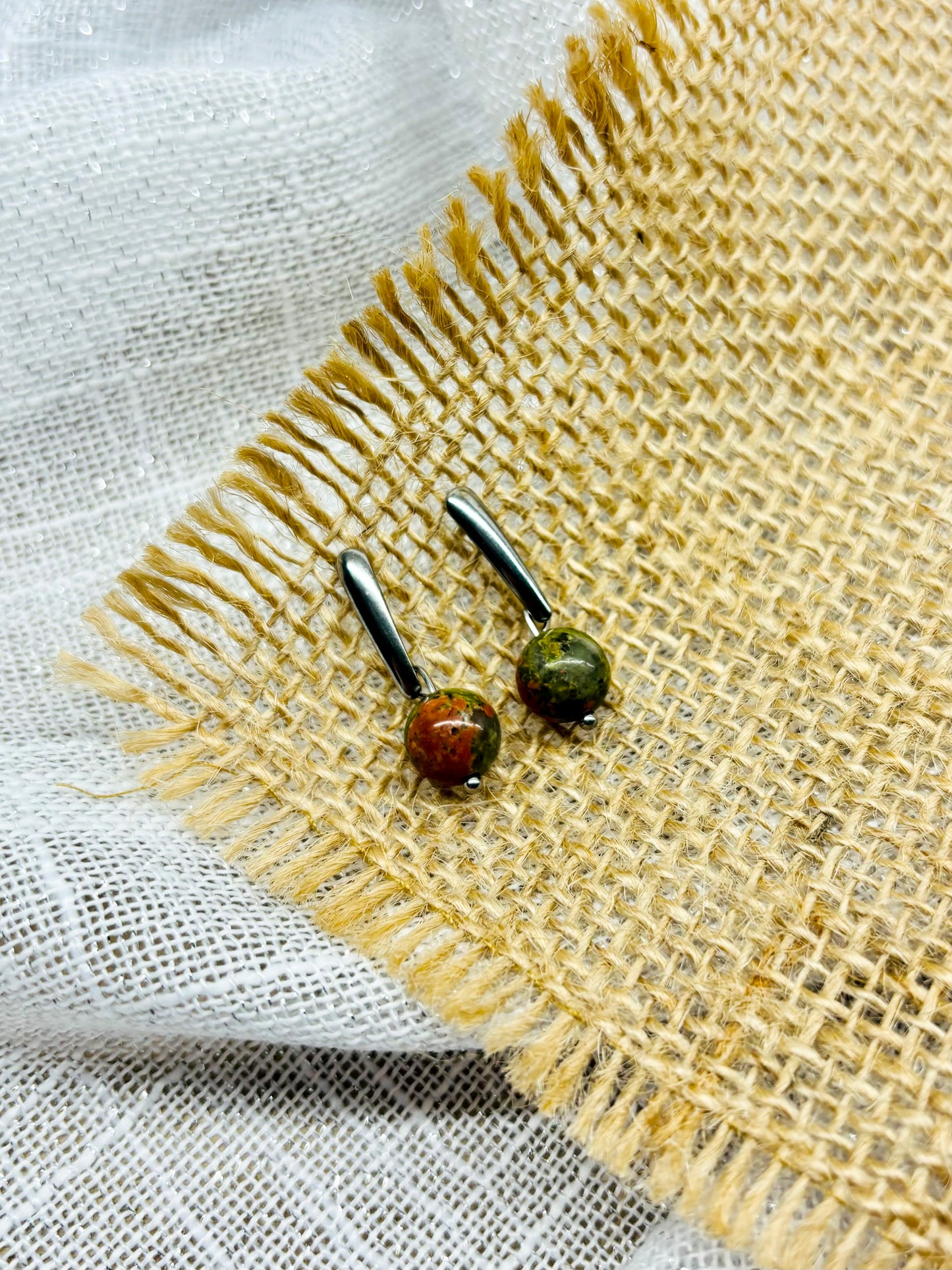 Boucles d'oreille MADELEINE, avec pierre d'Unakite, exposées sur de la toile de jute.