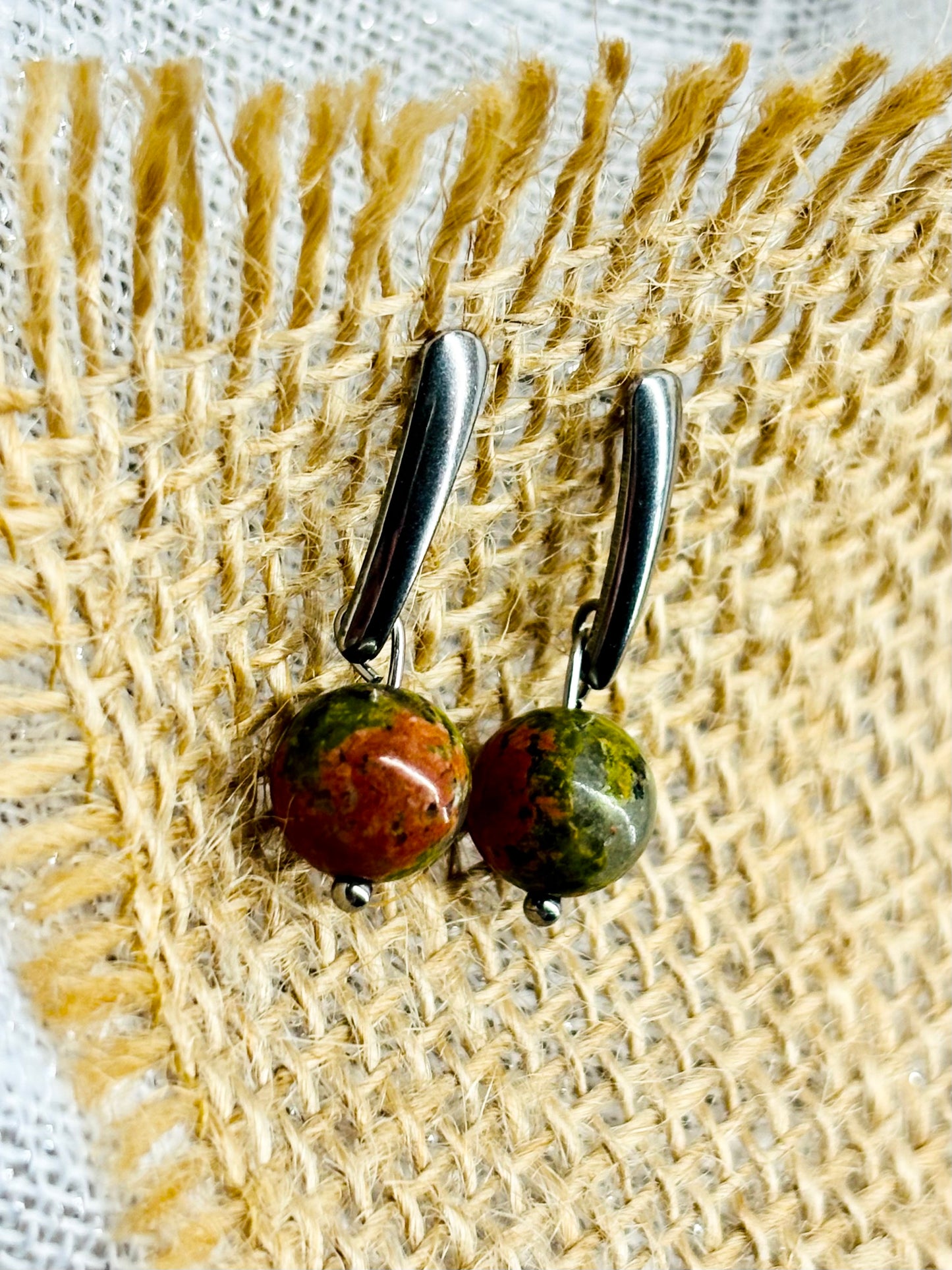 Boucles d'oreille MADELEINE, avec pierre d'Unakite, exposées sur de la toile de jute.