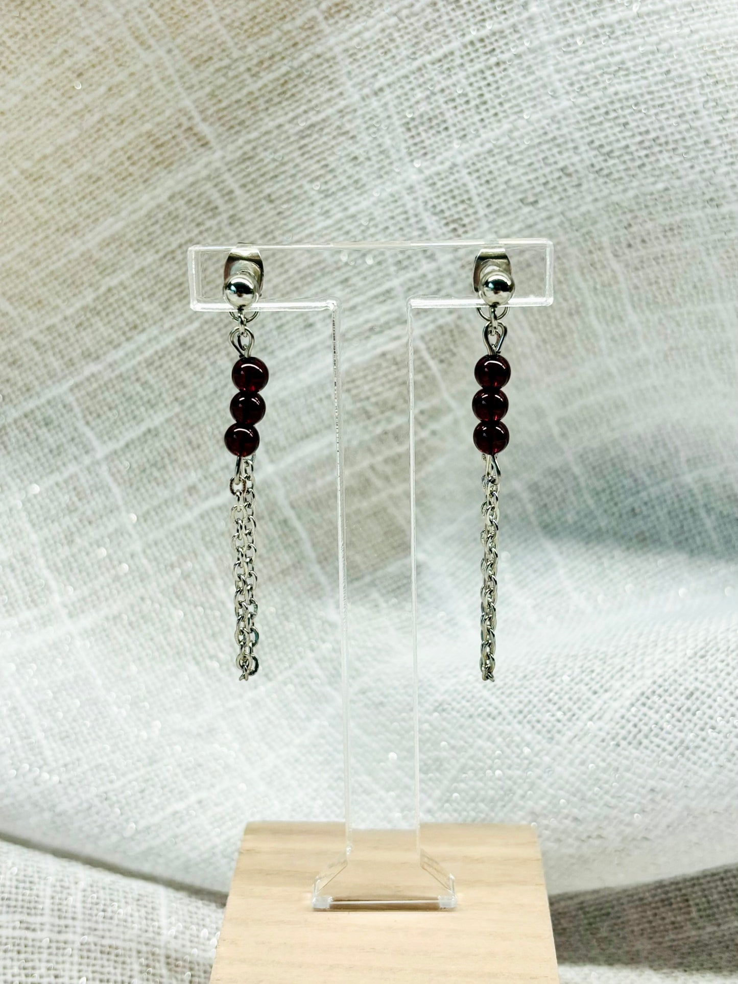 Boucles d'oreille MALIA, de couleur argent, exposées devant un fond en lin.