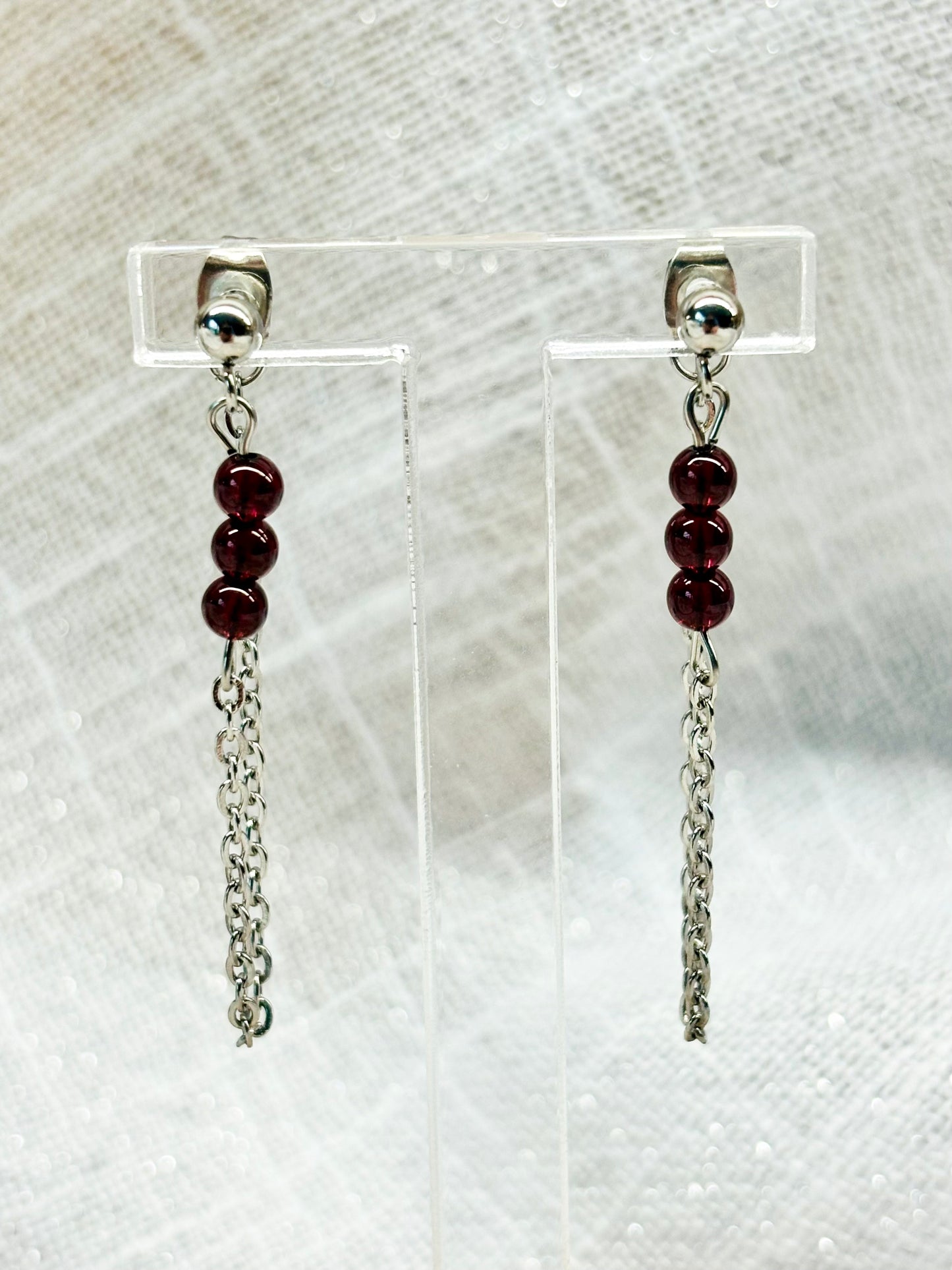 Boucles d'oreille MALIA, de couleur argent, exposées devant un fond en lin.