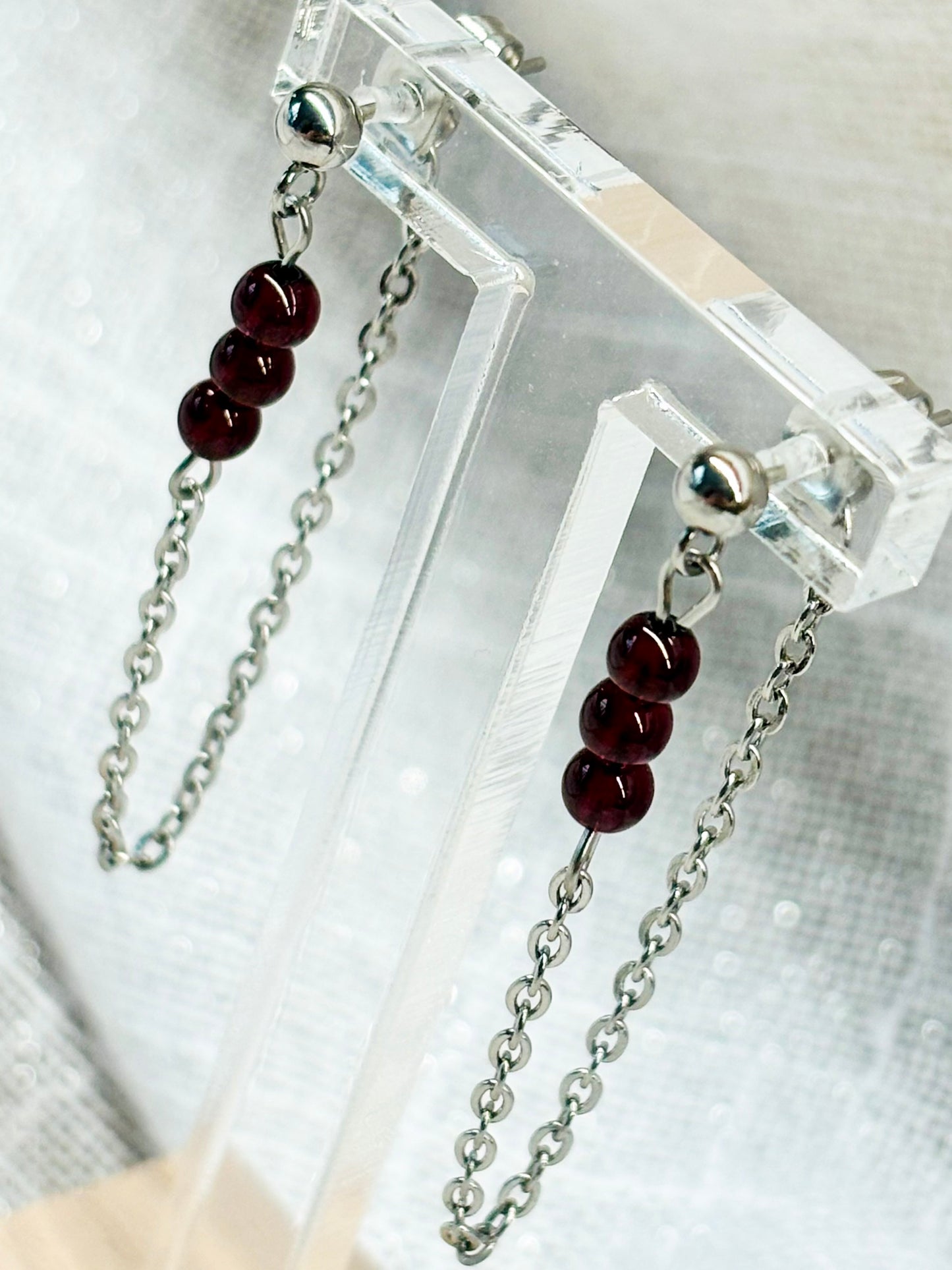 Boucles d'oreille MALIA, de couleur argent, exposées devant un fond en lin.