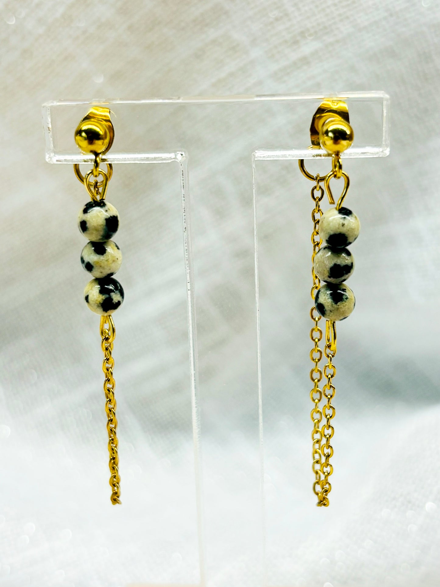 Boucles d'oreille MALIA, de couleur dorée avec pierre de Jaspe Dalmatien, exposées devant un fond en lin.