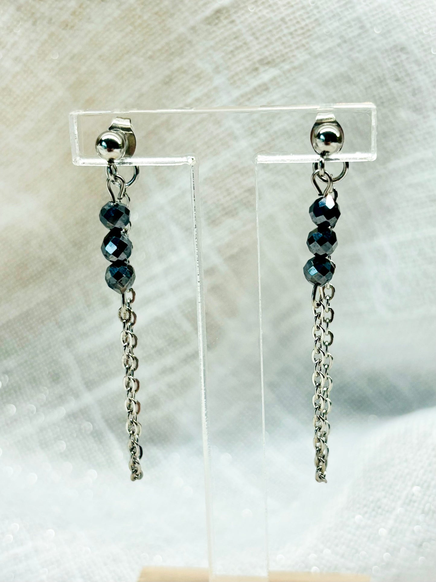 Boucles d'oreille MALIA, de couleur argent avec pierre de Térahertz, exposées devant un fond en lin.