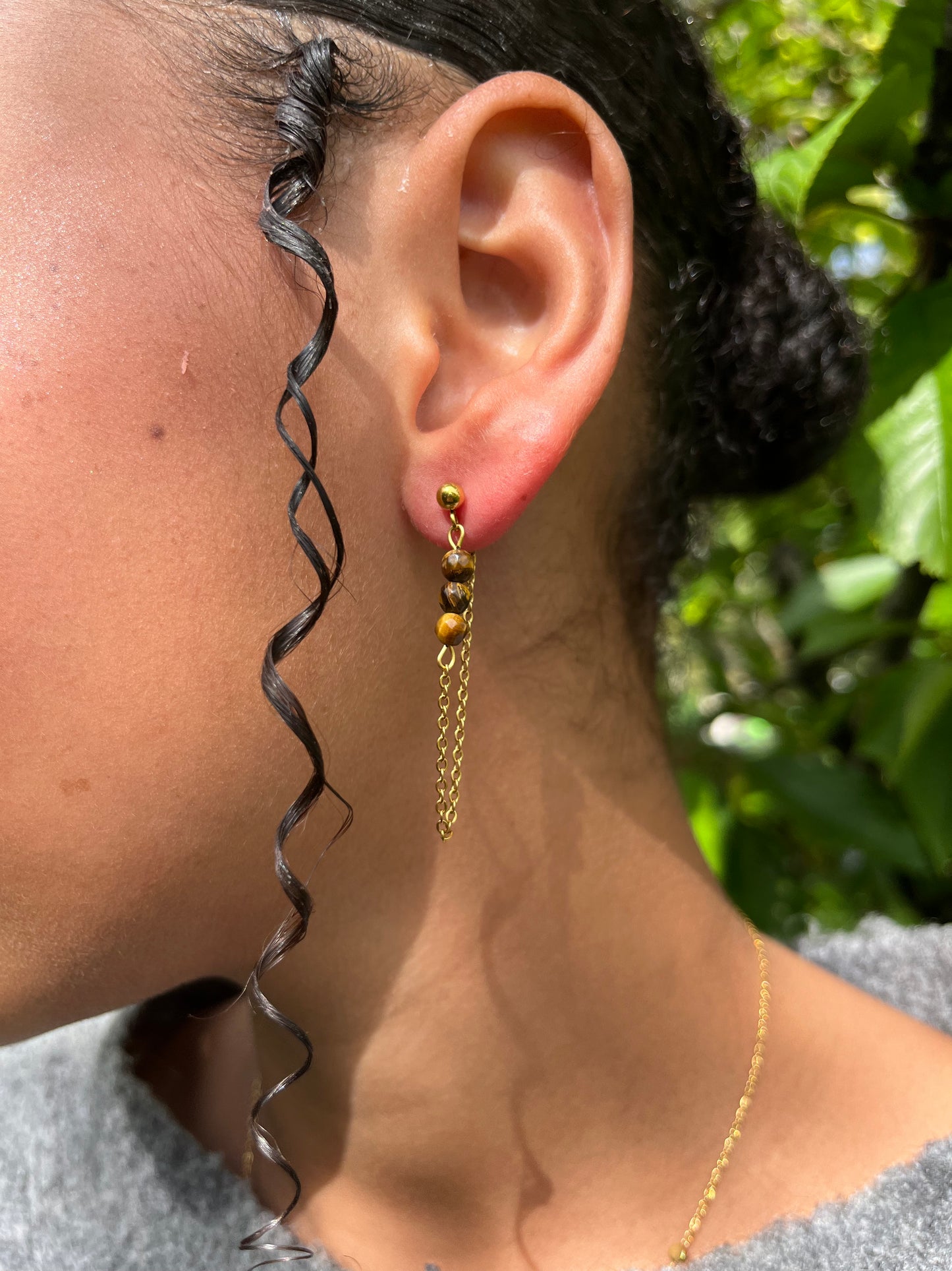 Boucles d'oreille MALIA, de couleur dorée avec pierre d'oeil de Tigre, portées.