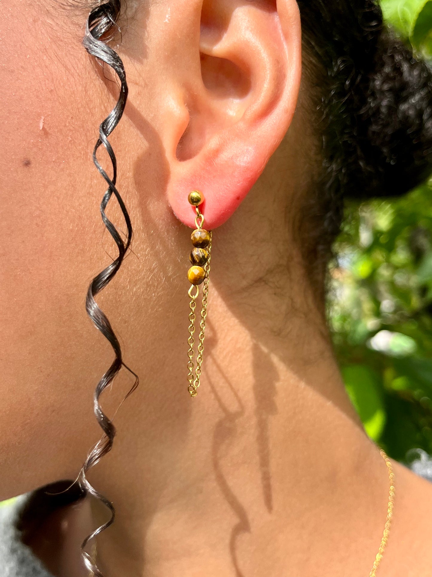 Boucles d'oreille MALIA, de couleur dorée avec pierre d'oeil de Tigre, portées.