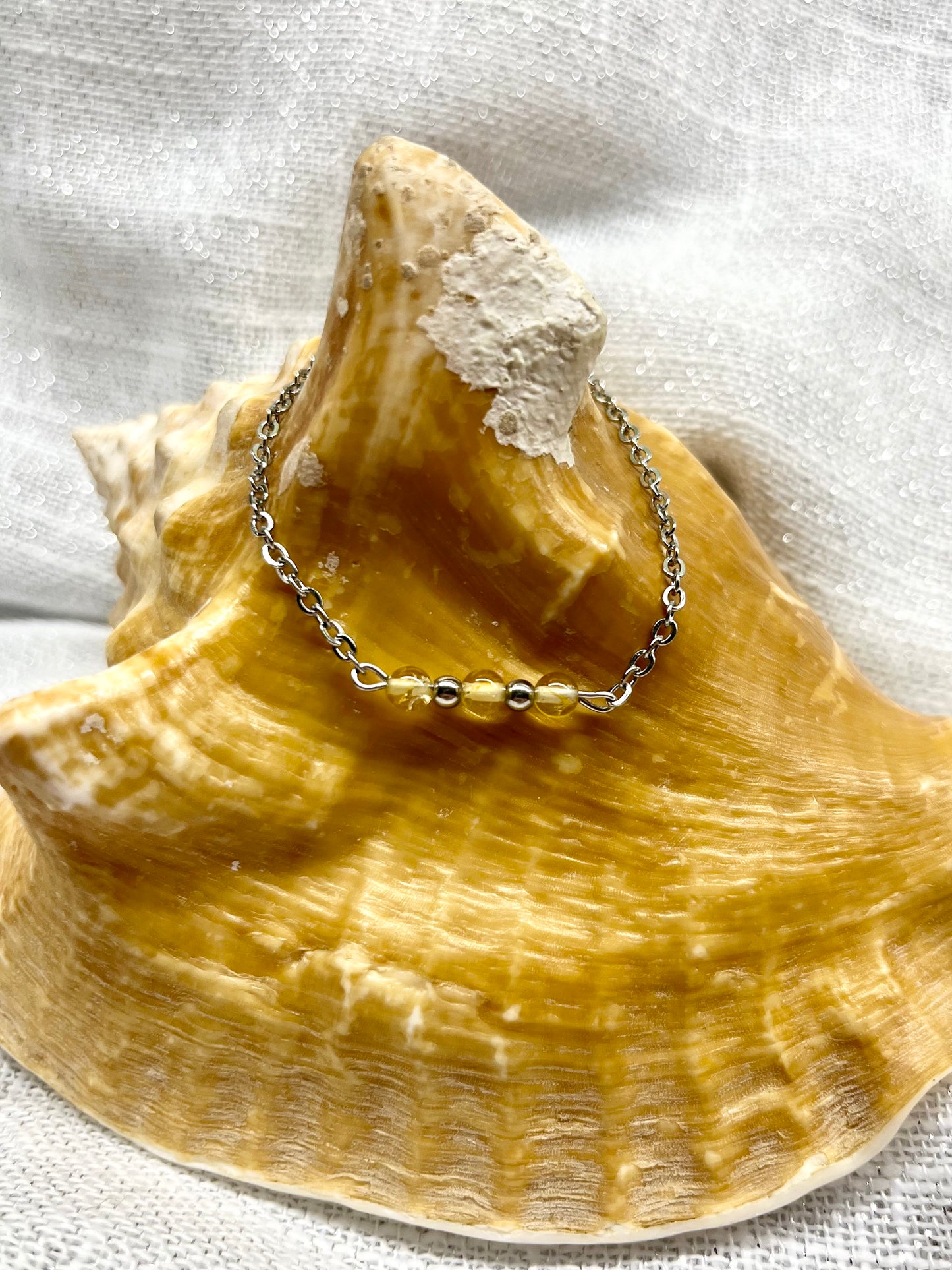 Bracelet MALIA, de couleur argent avec pierres de Citrine, exposé sur un coquillage.
