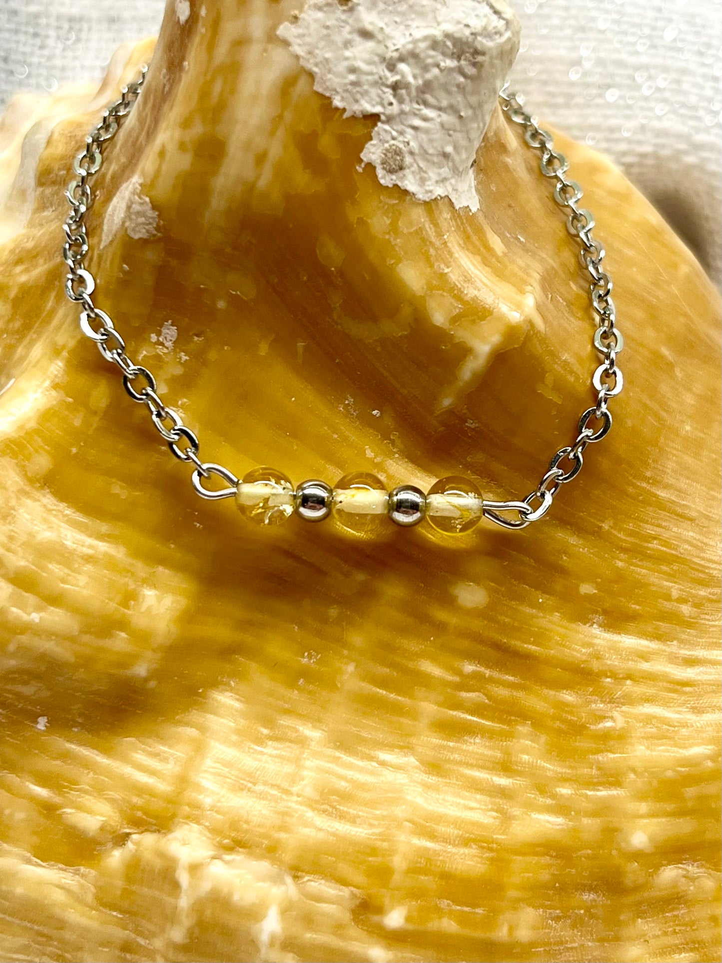 Bracelet MALIA, de couleur argent avec pierres de Citrine, exposé sur un coquillage.