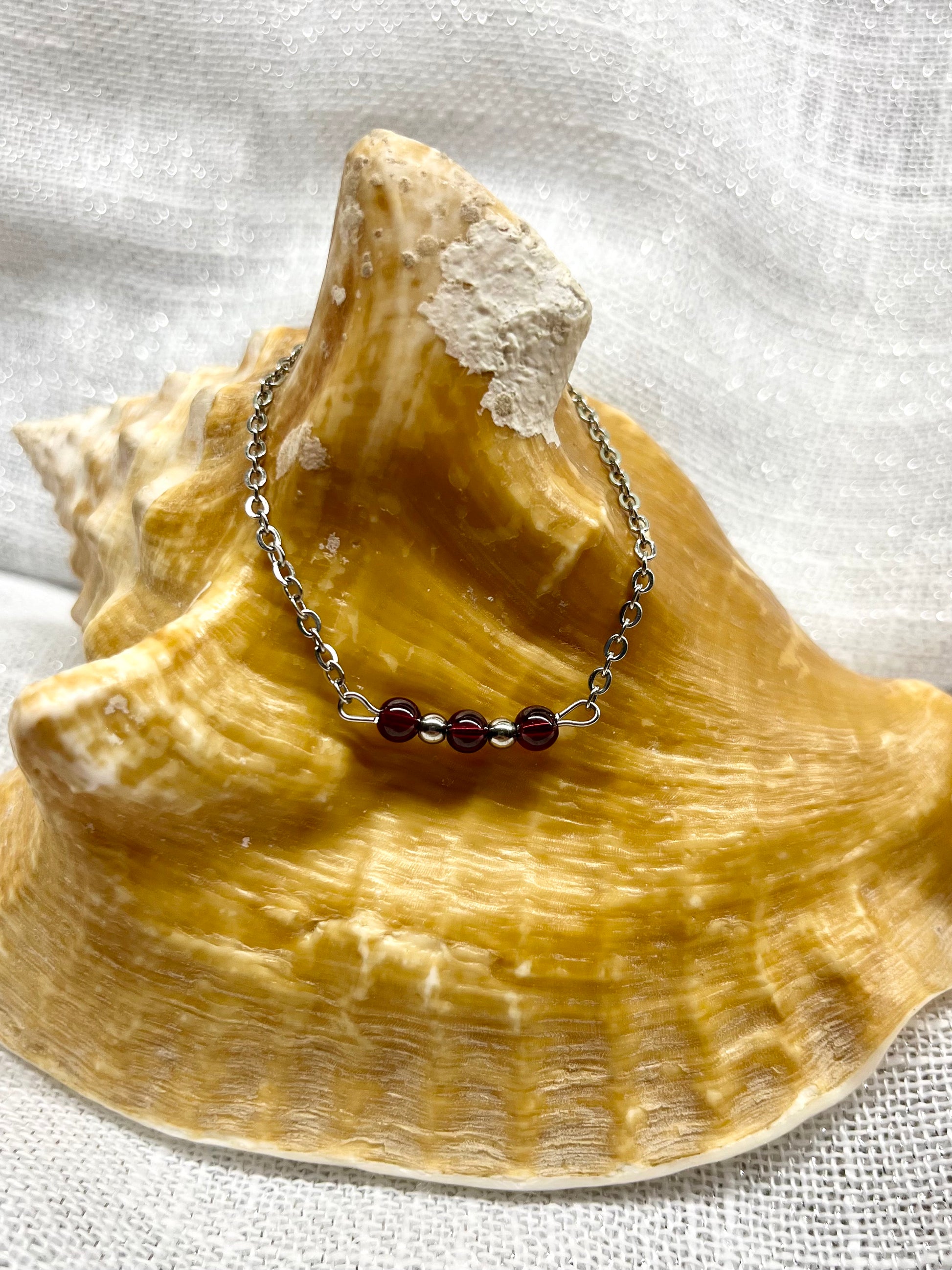 Collier MALIA, de couleur argent avec pierres de Grenat, exposé sur un coquillage.
