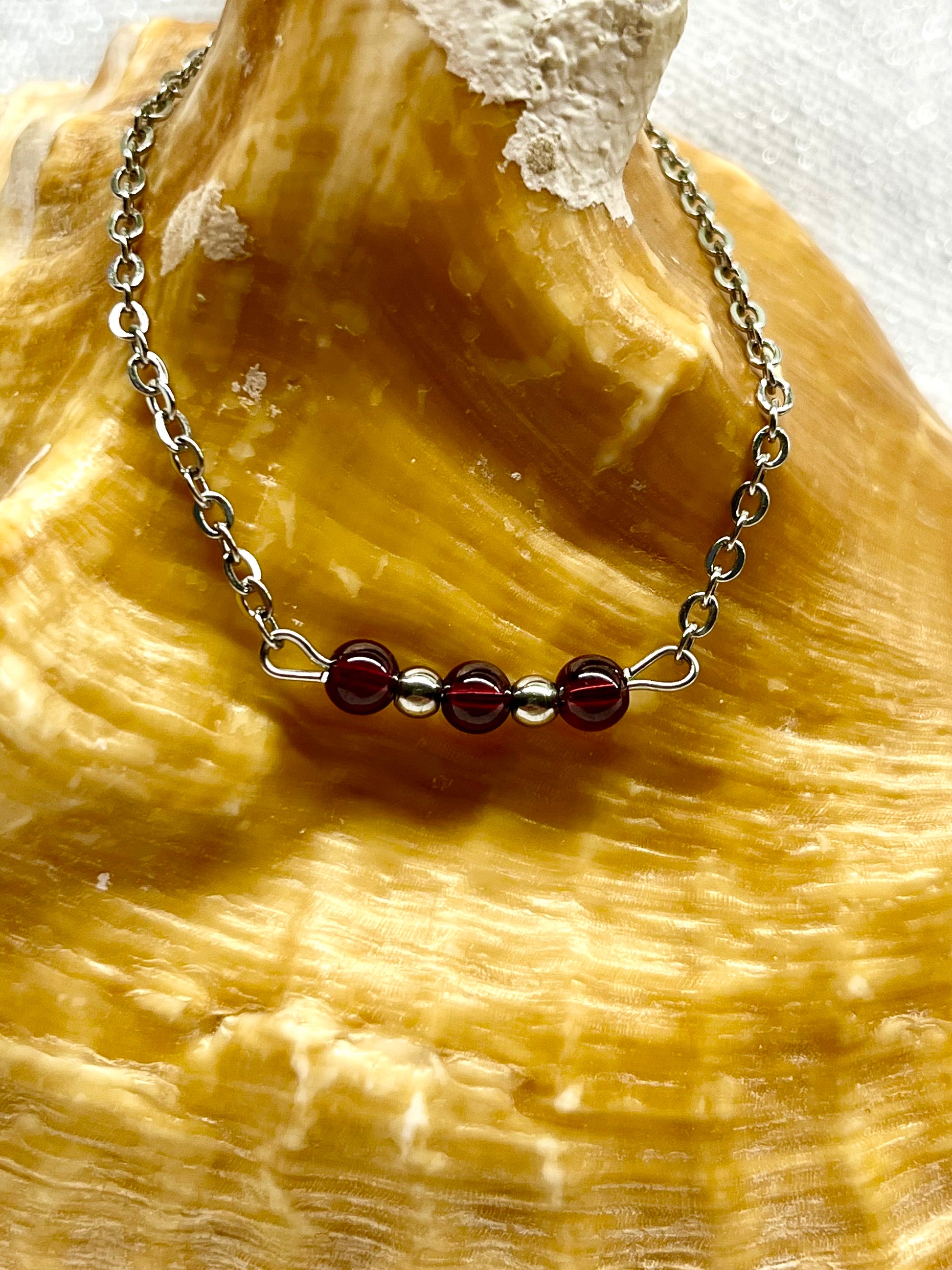 Collier MALIA, de couleur argent avec pierres de Grenat, exposé sur un coquillage.