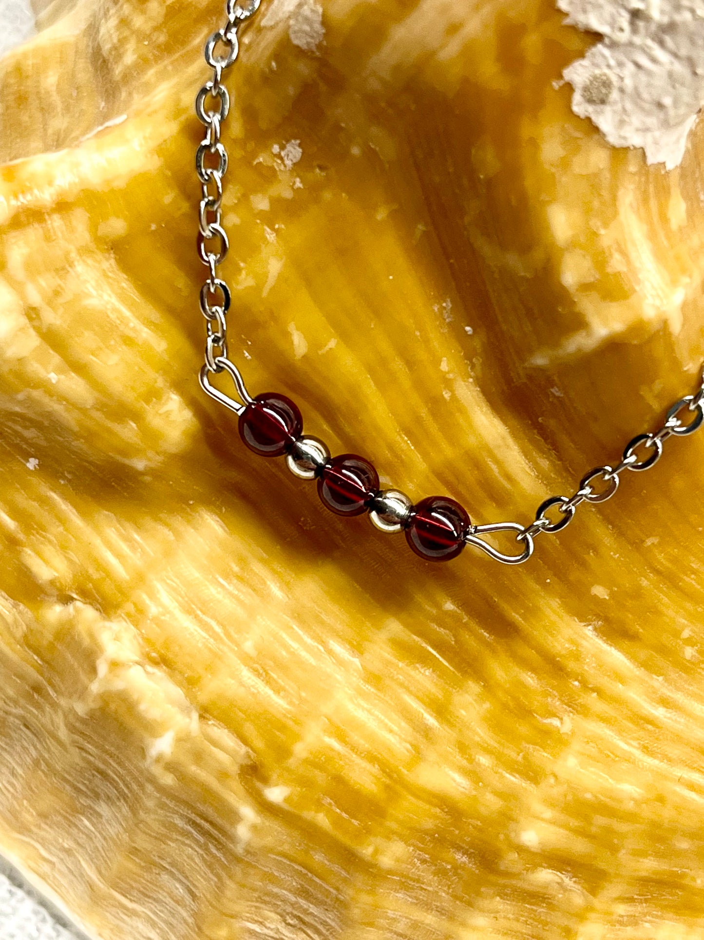 Collier MALIA, de couleur argent avec pierres de Grenat, exposé sur un coquillage.