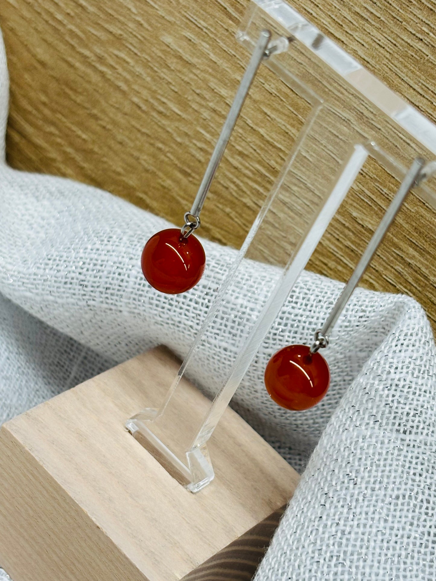 Boucles d'oreille MANON en pierre de Cornaline, exposées sur un fond en bois et lin.