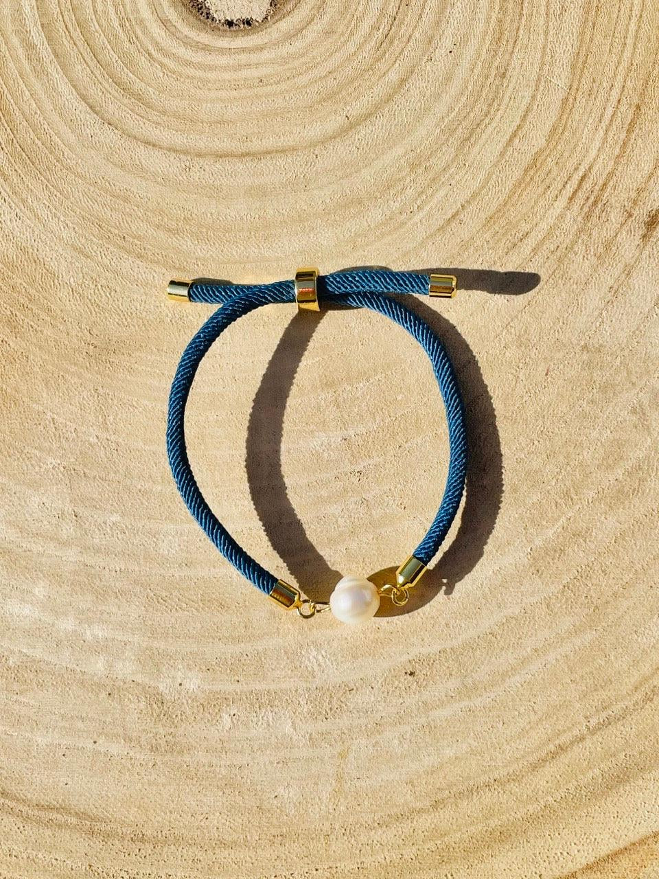 Bracelet MIA, avec cordon de couleur bleu jean et perle de culture, exposé sur un fond en bois.