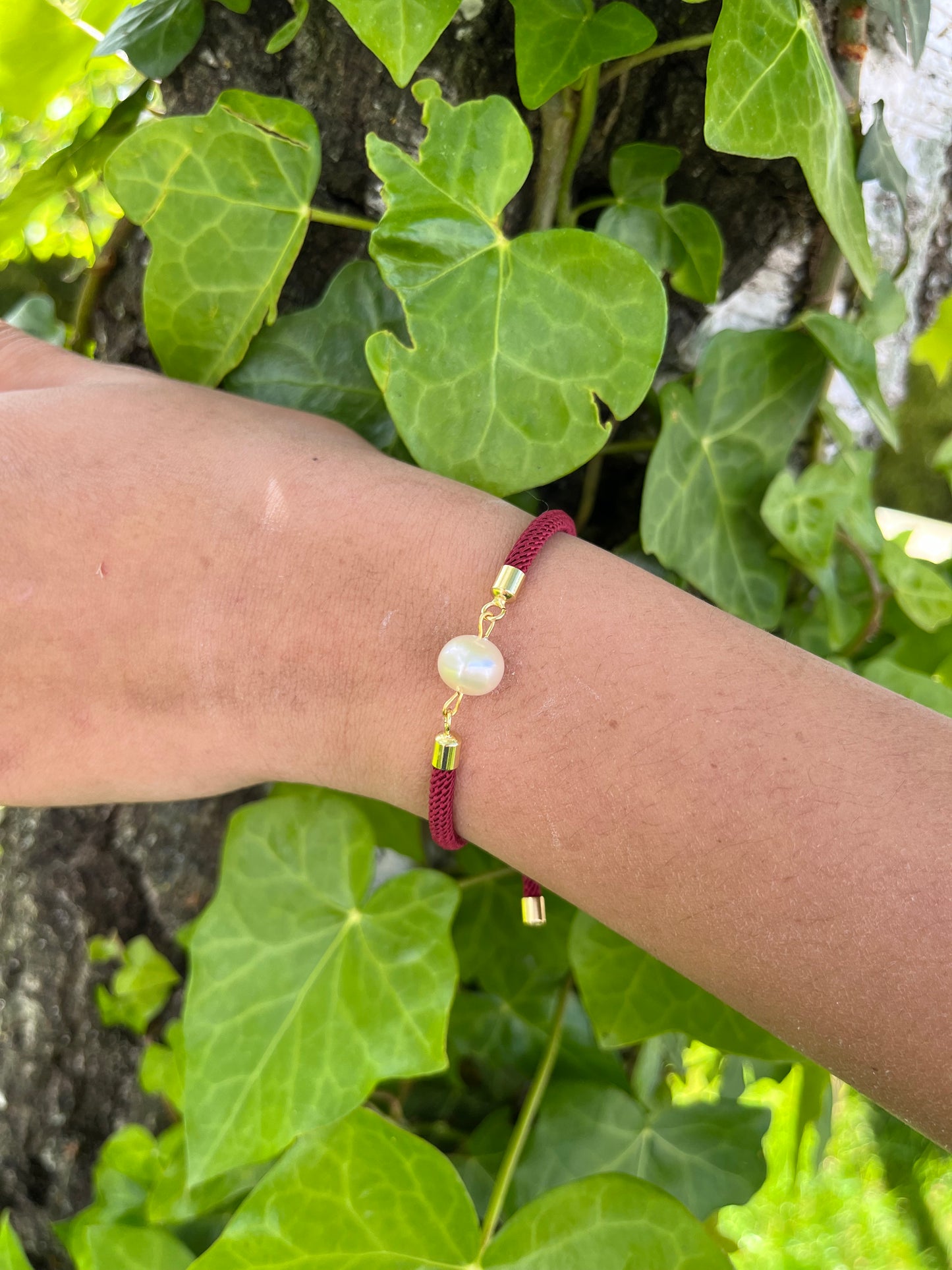 Bracelet MIA avec cordon de couleur rose fluo et perle de culture, porté sur un poignet de femme sur un fond de feuilles.