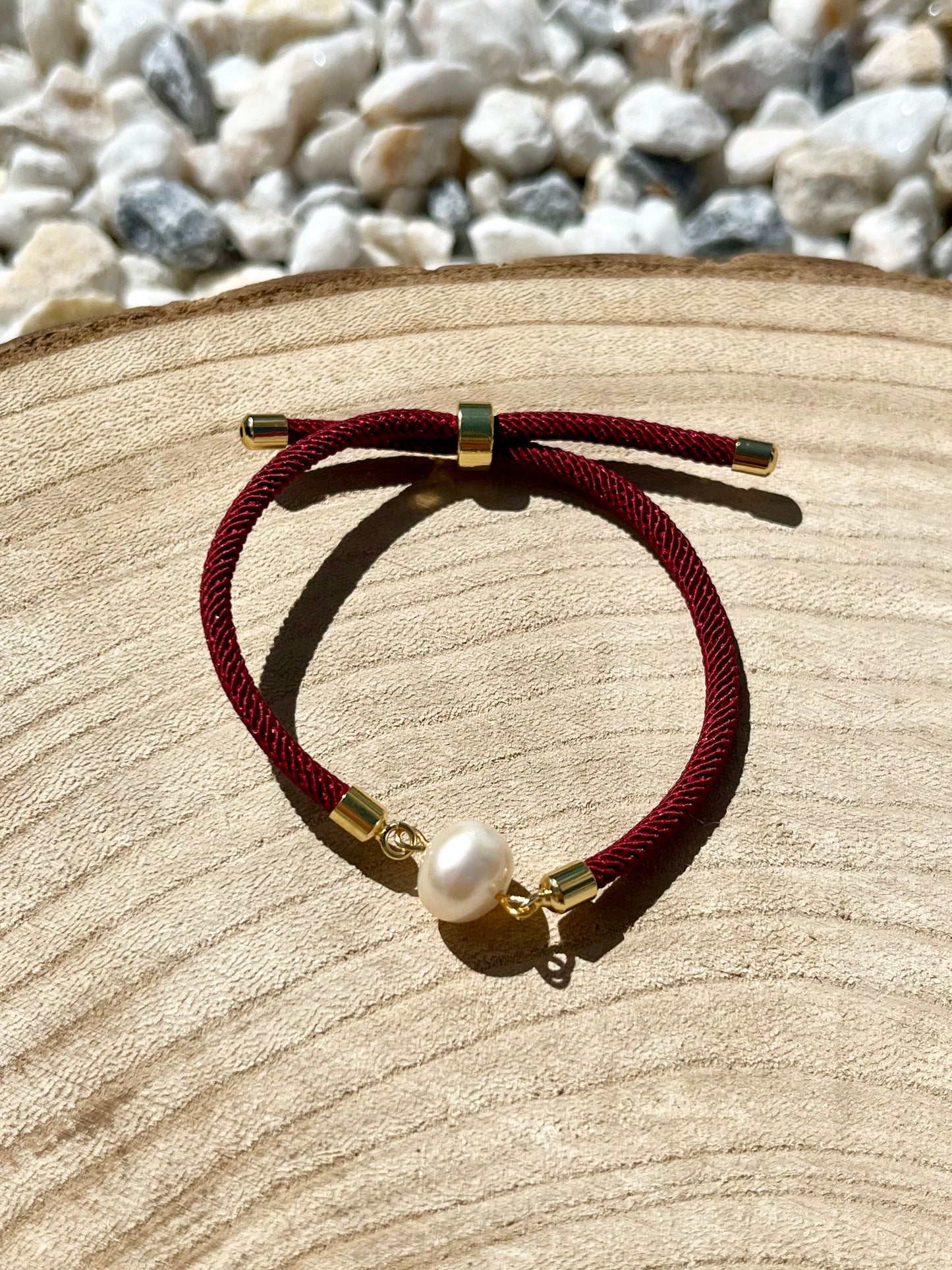 Bracelet MIA avec cordon de couleur rose fluo et perle de culture, exposé sur un fond en bois.