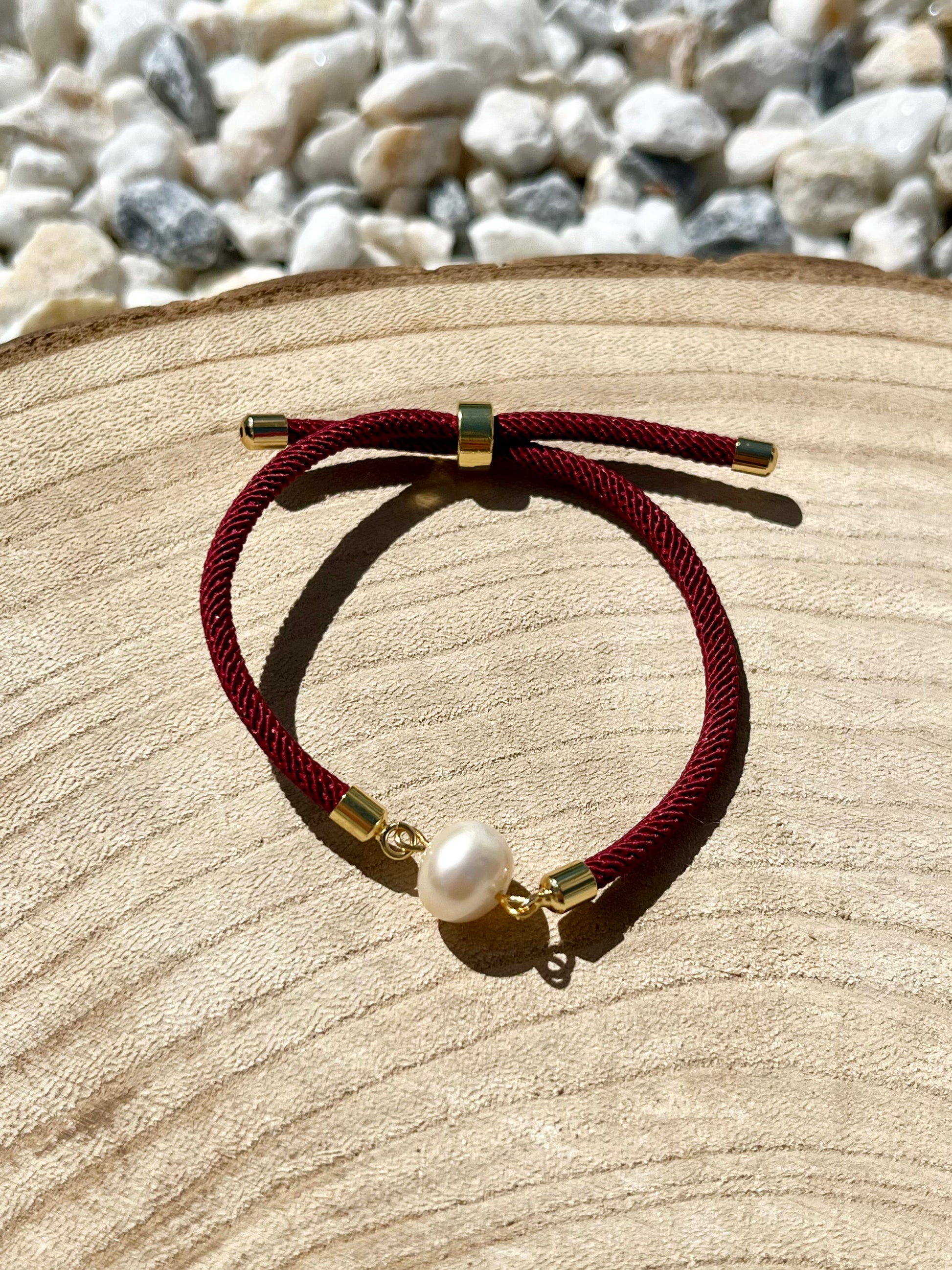 Bracelet MIA avec cordon de couleur rose fluo et perle de culture, exposé sur un fond en bois.