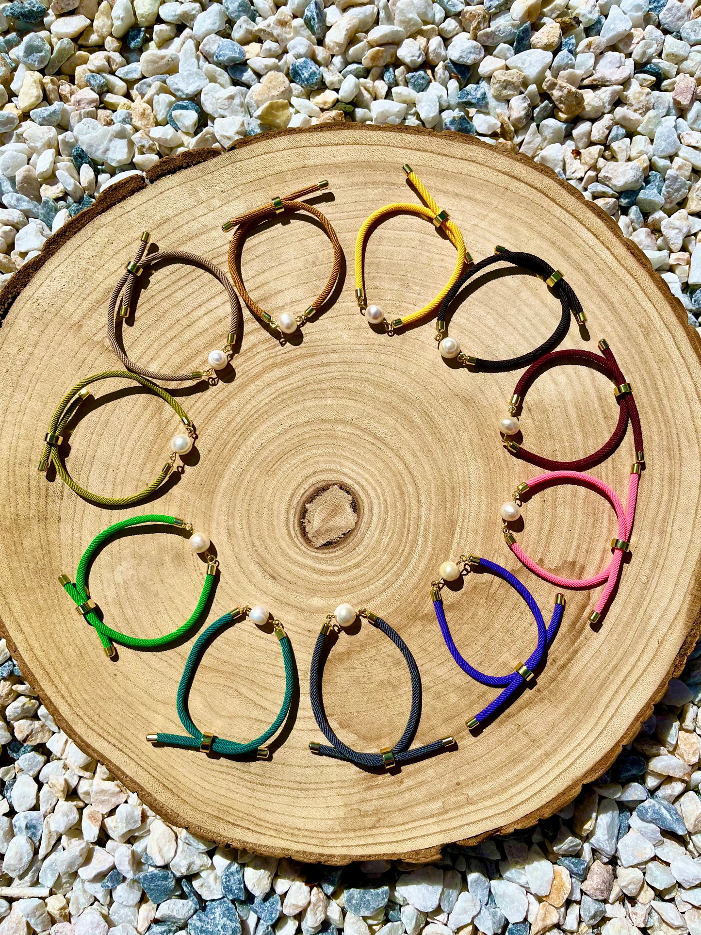 Bracelets MIA, avec cordon et perle de culture, exposé sur un fond en bois et graviers blancs.