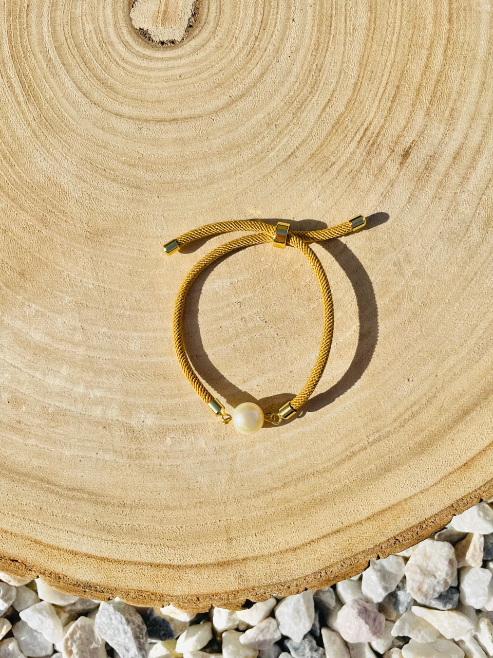 Bracelet MIA, avec cordon de couleur sable et perle de culture, exposé sur un fond en bois.