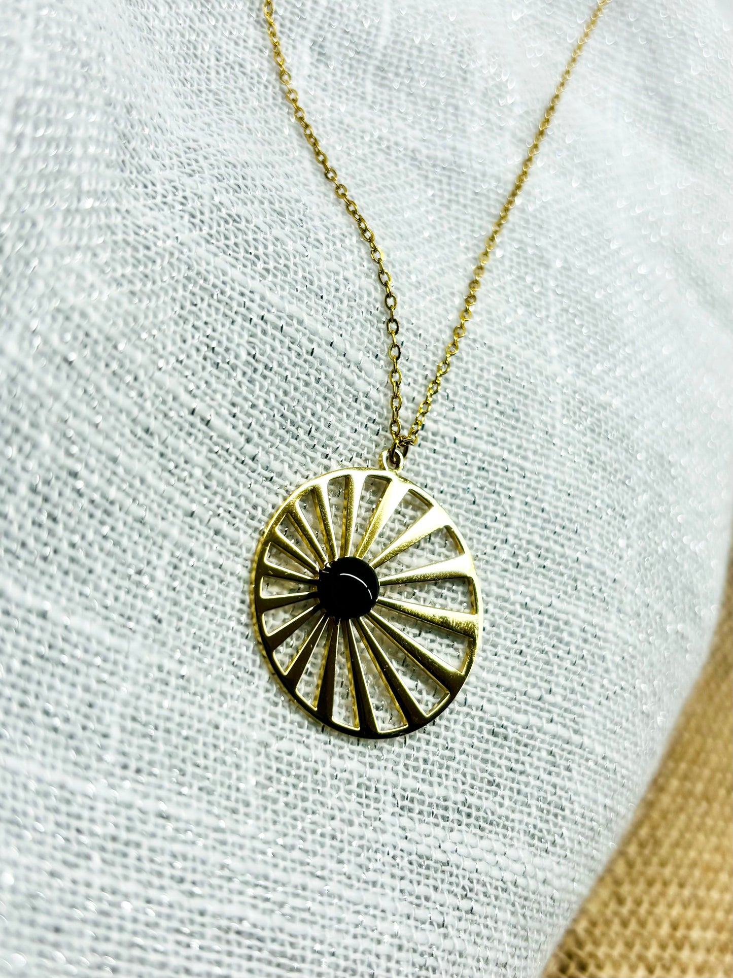 Collier SANA, de couleur dorée avec pierre d'Agate, exposé sur un fond en lin.