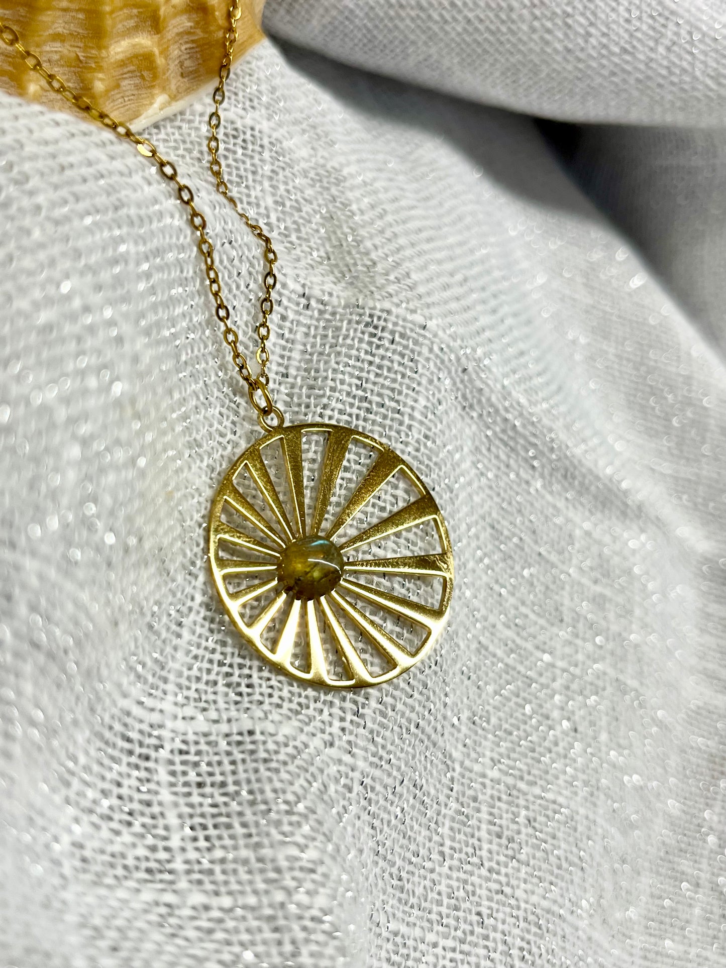 Collier SANA, de couleur dorée avec pierre de Labradorite, exposé sur un fond en lin.