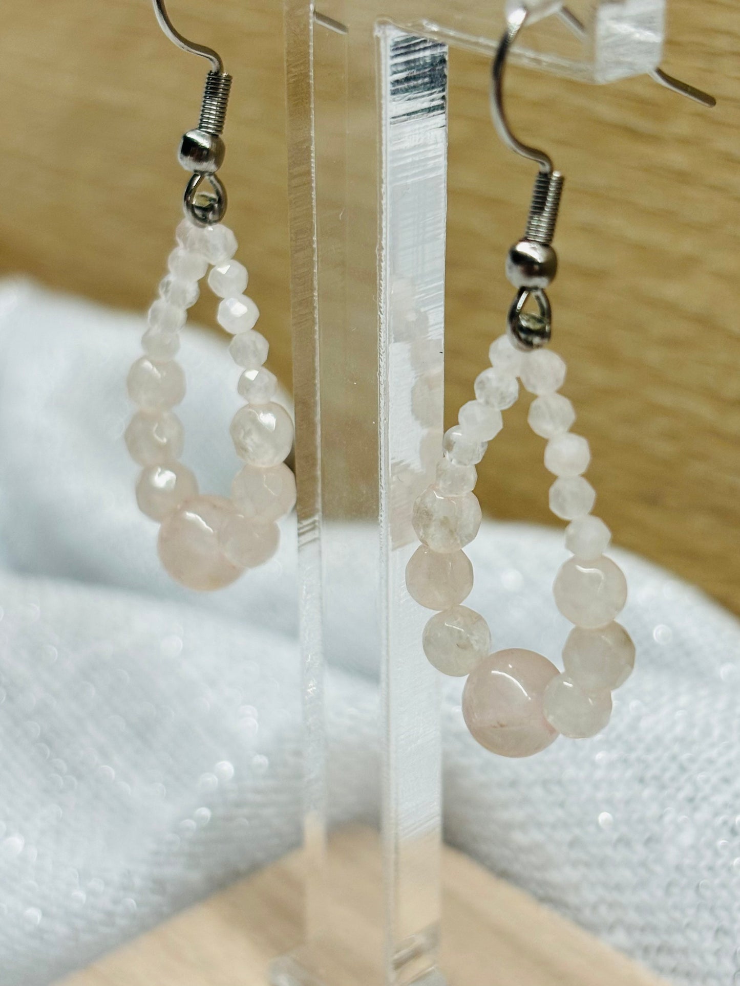 Boucles d'oreille SIMONA, avec pierres de Quartz Rose, exposées sur un fond en bois.