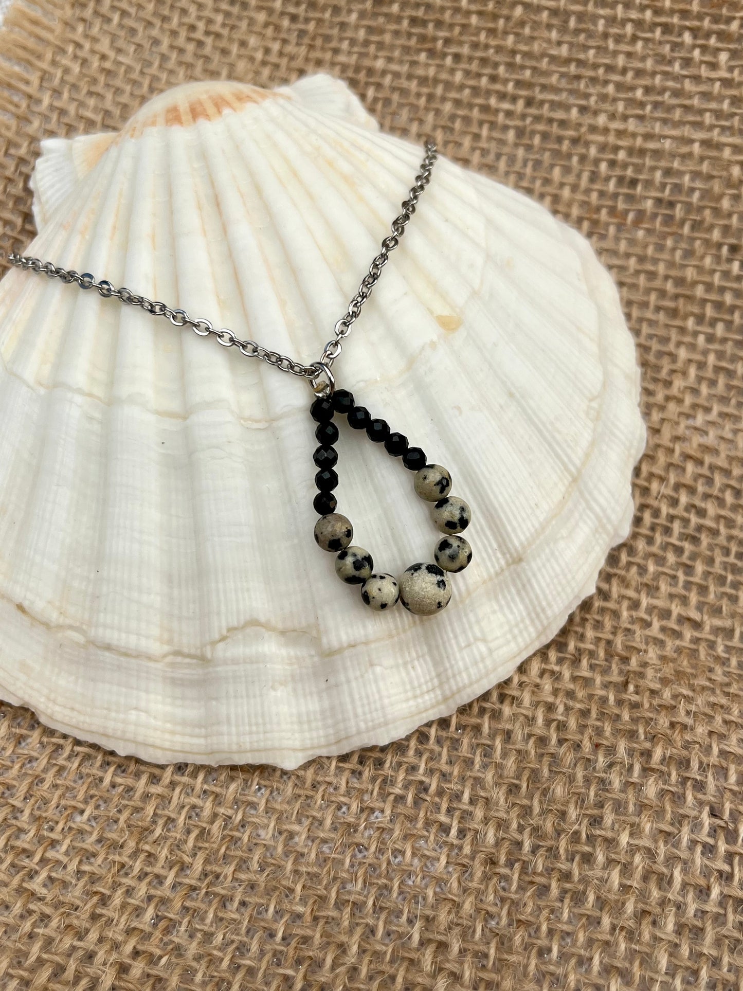 Collier SIMONA, avec pierres de Jaspe Dalmatien et de Tourmaline Noire, exposé sur un coquillage.