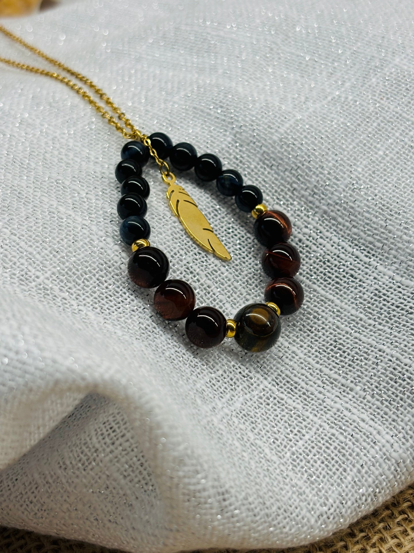 Collier SIMONE, avec pierre d'Oeil de Tigre, de Taureau et de Faucon, exposé sur un fond en lin.