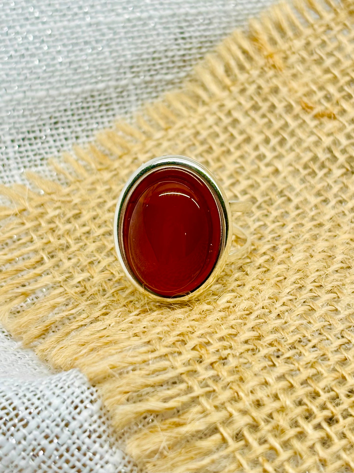 Bague THÉA, en argent et pierre de Cornaline, sur un fond de lin et toile de jute.
