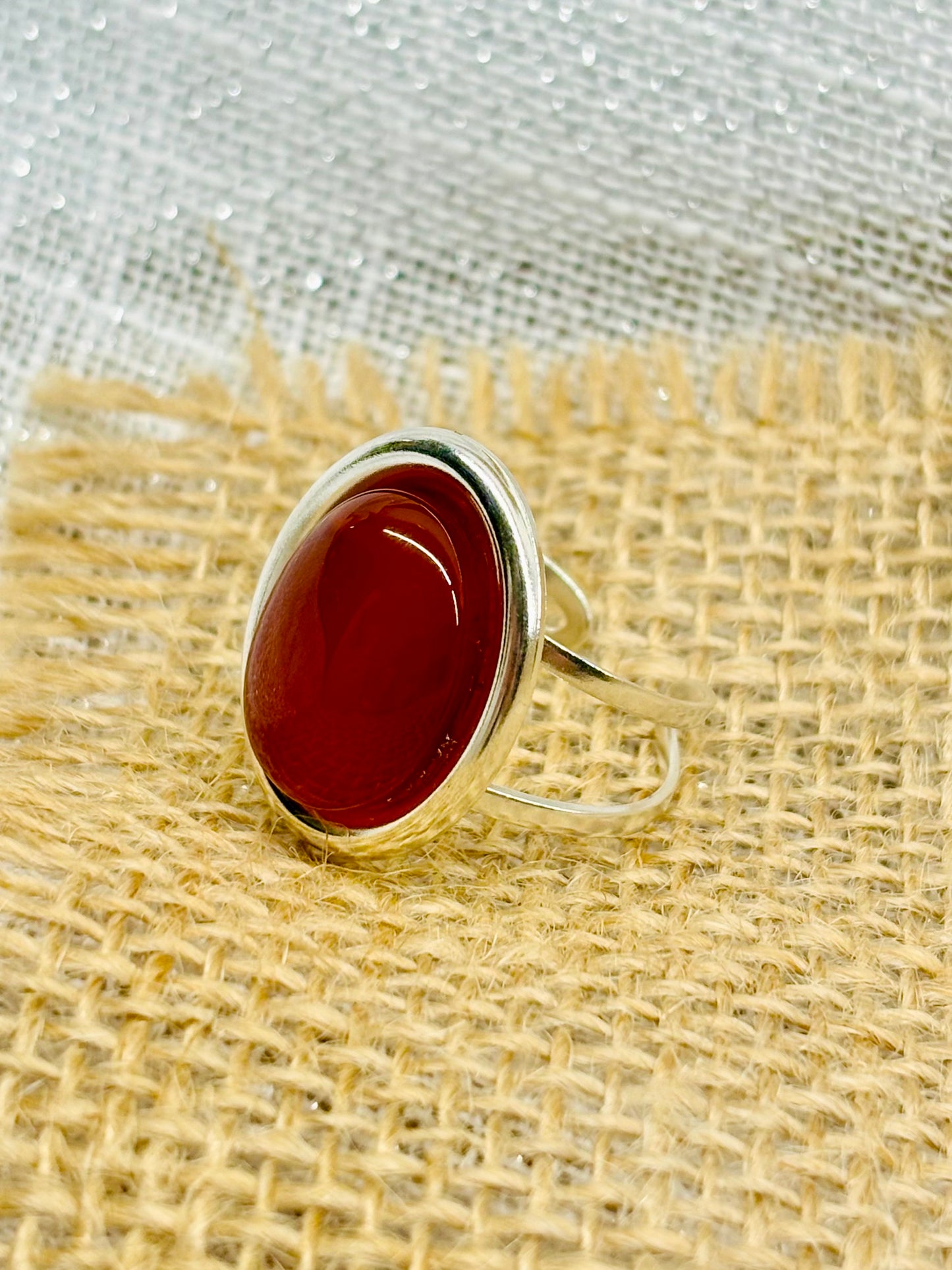 Bague THÉA, en argent et pierre de Cornaline, sur un fond de lin et toile de jute.