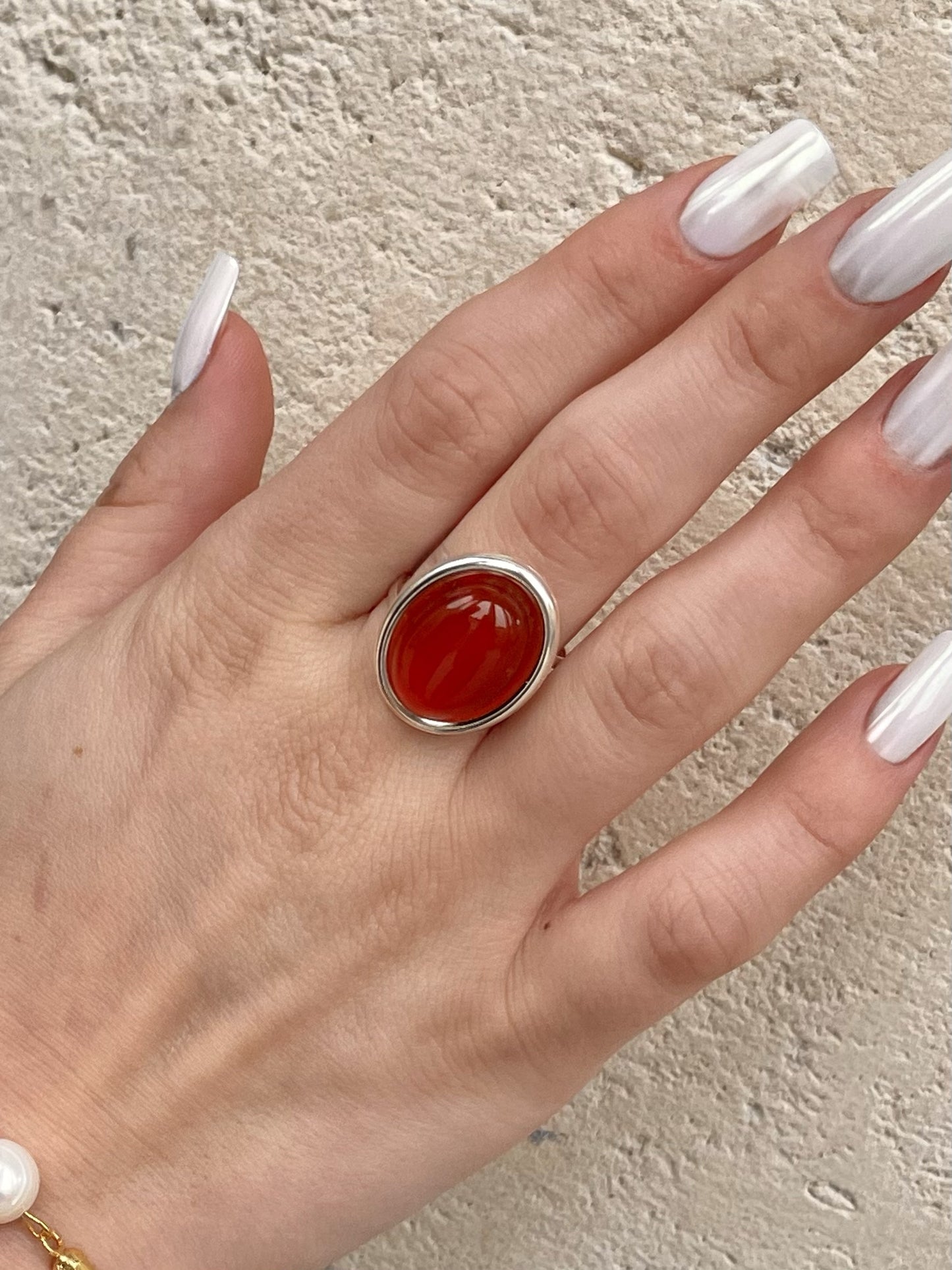 Bague THÉA, en argent et pierre de Cornaline, portée sur une main de femme.