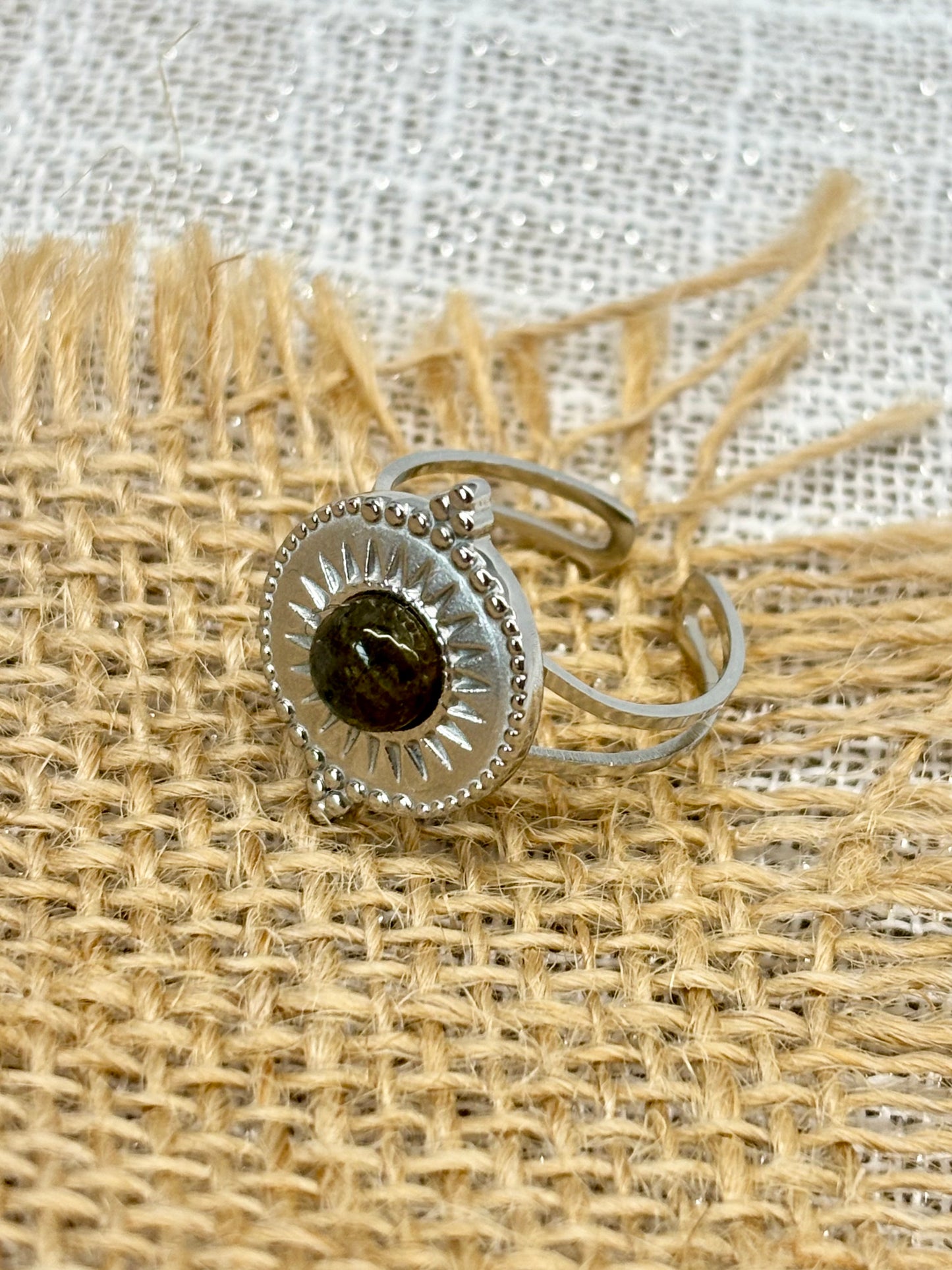 Gros plan de la Bague ZÉLIE en acier inoxydable argent, avec pierre de Labradorite, exposé sur de la toile de jute et fond en lin blanc.