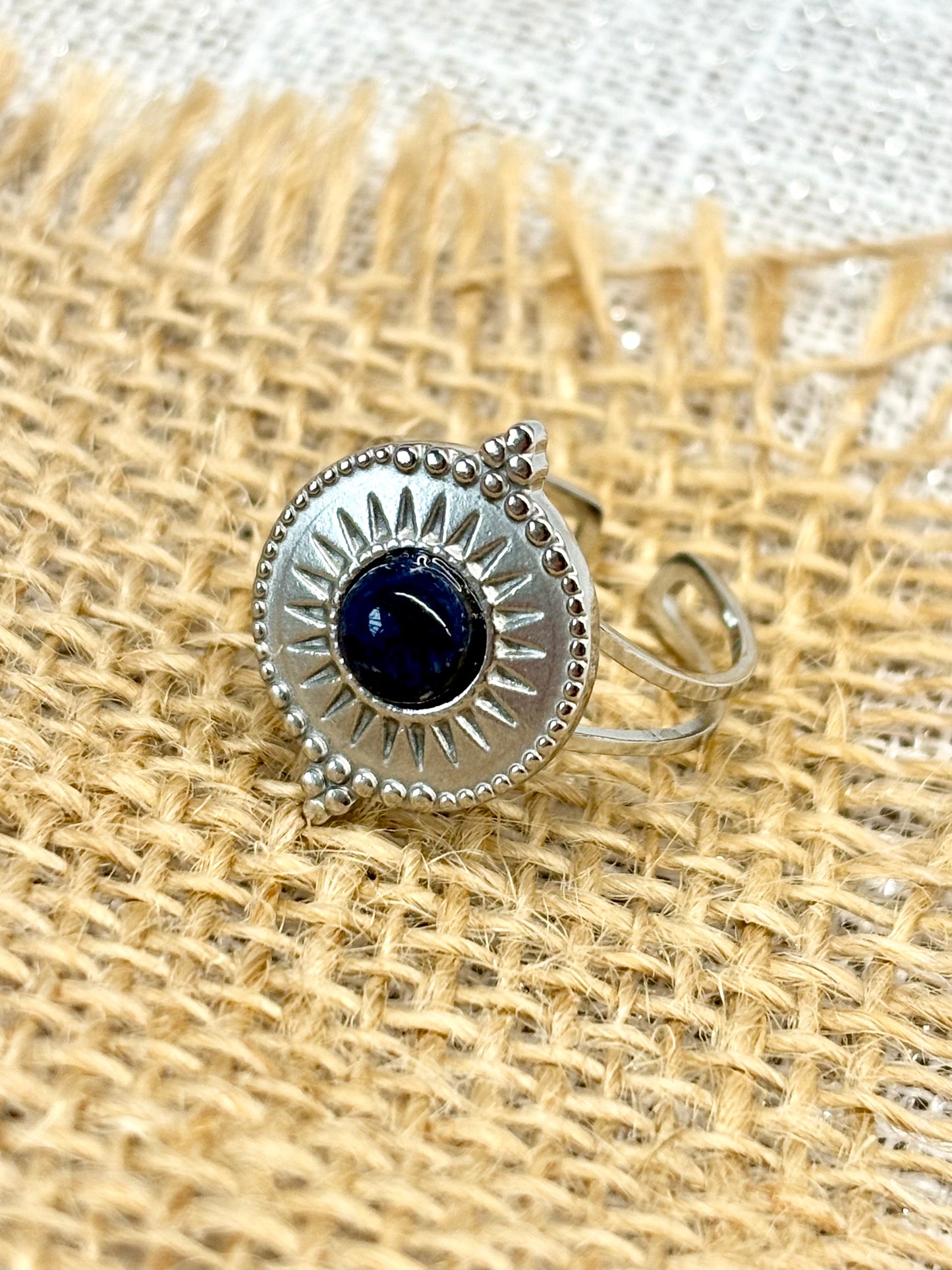 Gros plan de la Bague ZÉLIE en acier inoxydable argent et pierre de Sodalite, exposé sur de la toile de jute et un fond en lin.